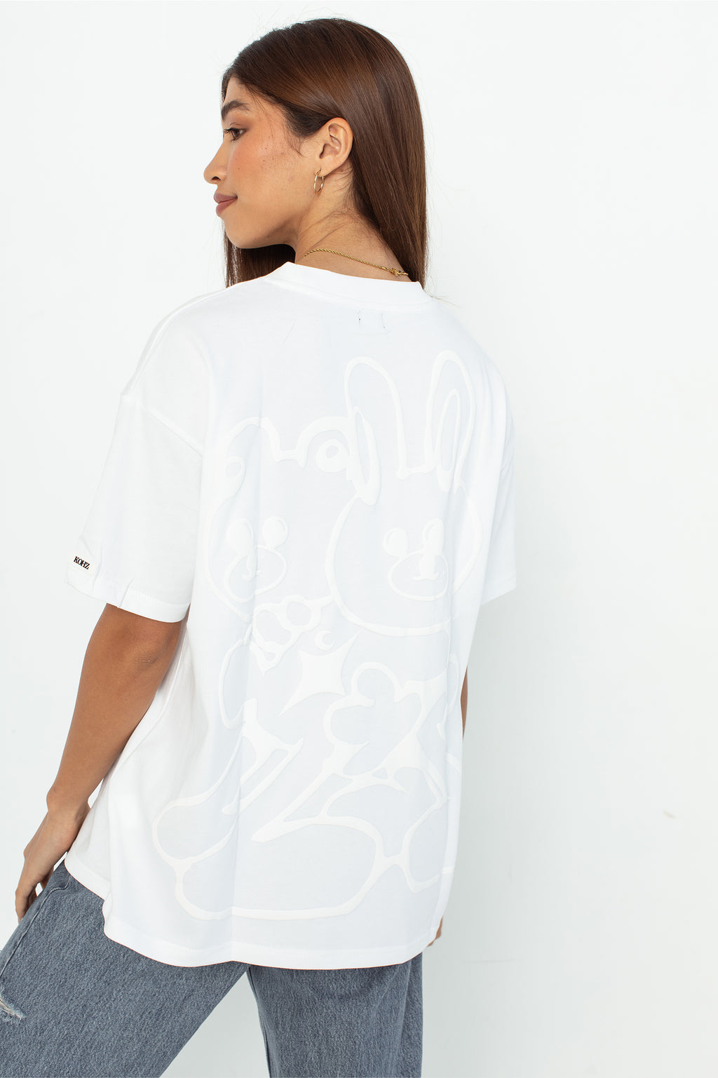 A model wearing a white oversized kohz bb t-shirt with a puff printed logo, crew neck, and short sleeves standing against a white background.