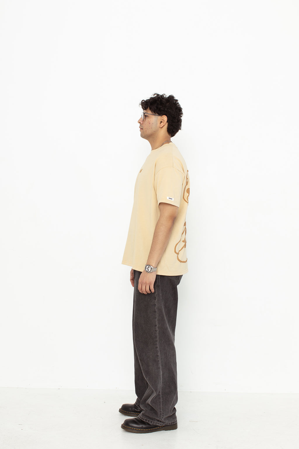 A model wearing a white oversized kohz bb t-shirt with a puff printed logo, crew neck, and short sleeves standing against a white background.