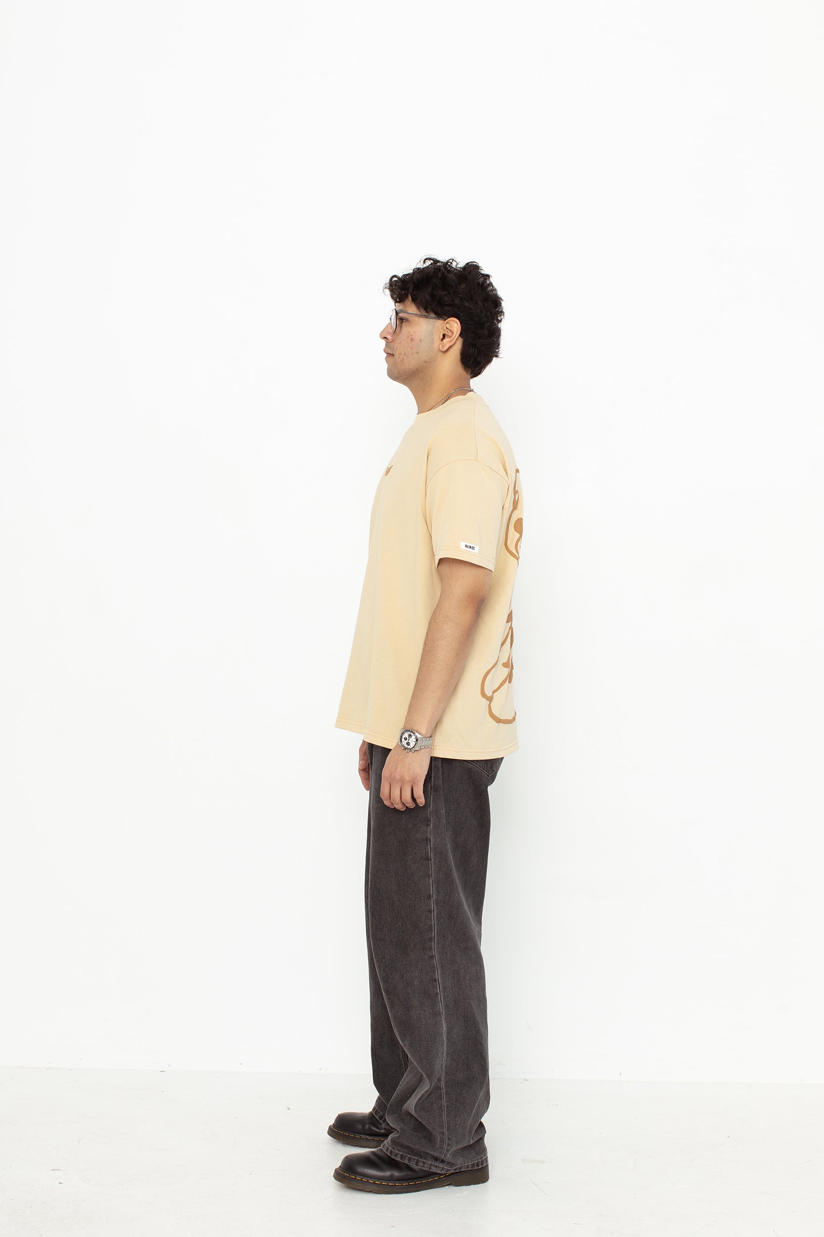 A model wearing a white oversized kohz bb t-shirt with a puff printed logo, crew neck, and short sleeves standing against a white background.
