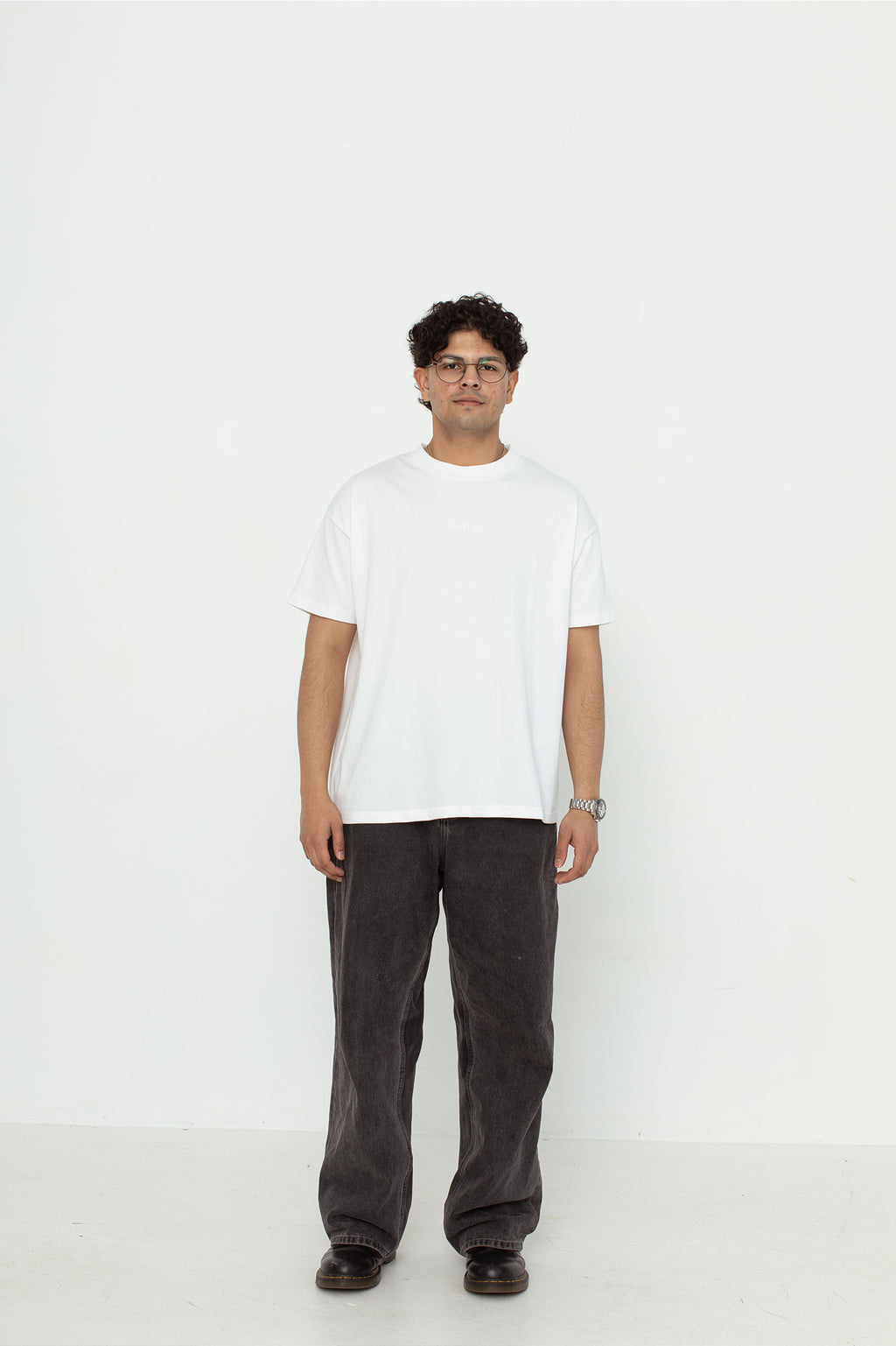 A model wearing a white oversized kohz bb t-shirt with a puff printed logo, crew neck, and short sleeves standing against a white background.