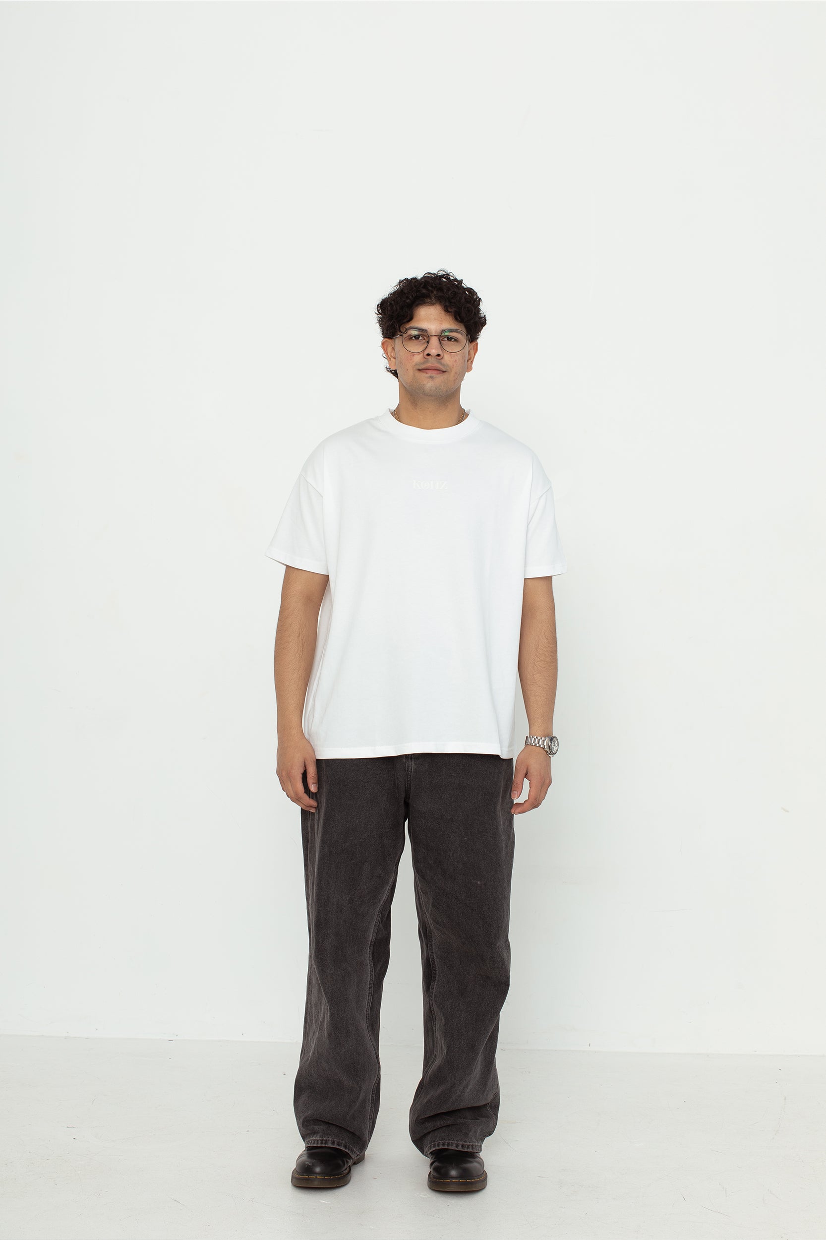 A model wearing a white oversized kohz bb t-shirt with a puff printed logo, crew neck, and short sleeves standing against a white background.