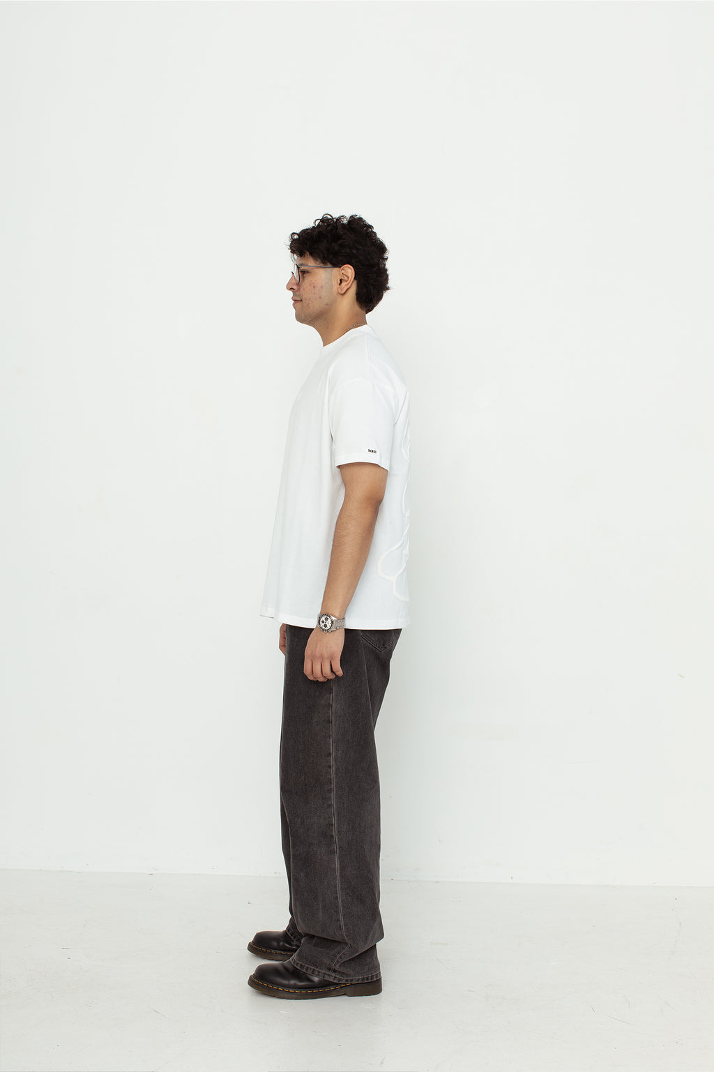 A model wearing a white oversized kohz bb t-shirt with a puff printed logo, crew neck, and short sleeves standing against a white background.