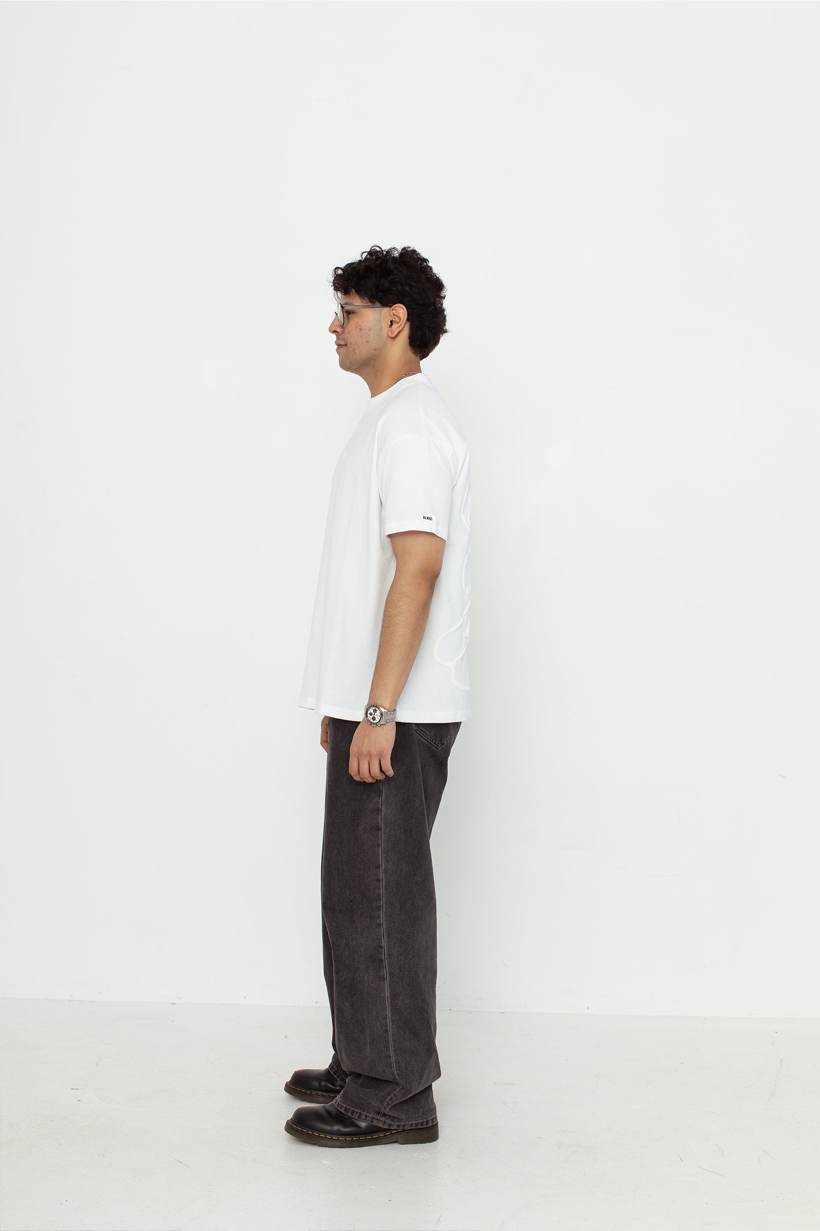 A model wearing a white oversized kohz bb t-shirt with a puff printed logo, crew neck, and short sleeves standing against a white background.