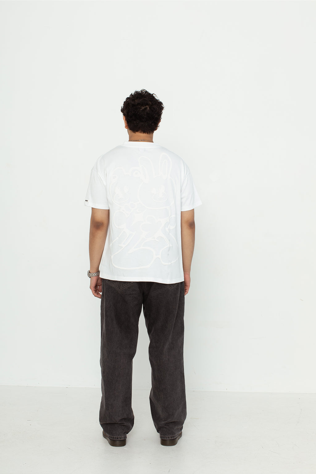 A model wearing a white oversized kohz bb t-shirt with a puff printed logo, crew neck, and short sleeves standing against a white background.