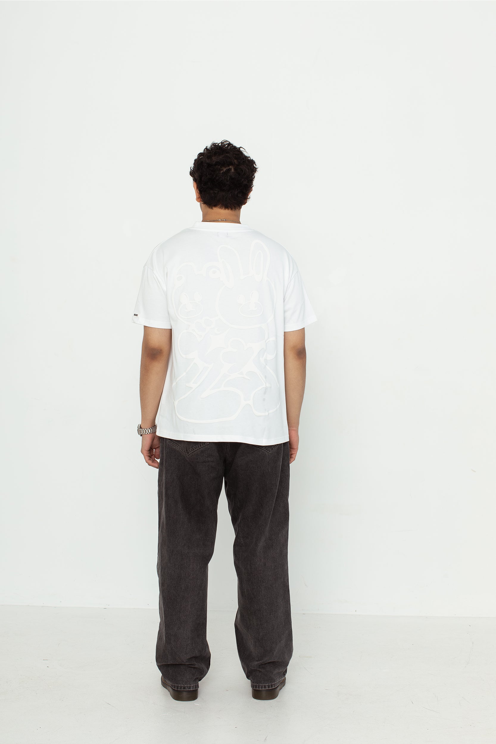 A model wearing a white oversized kohz bb t-shirt with a puff printed logo, crew neck, and short sleeves standing against a white background.