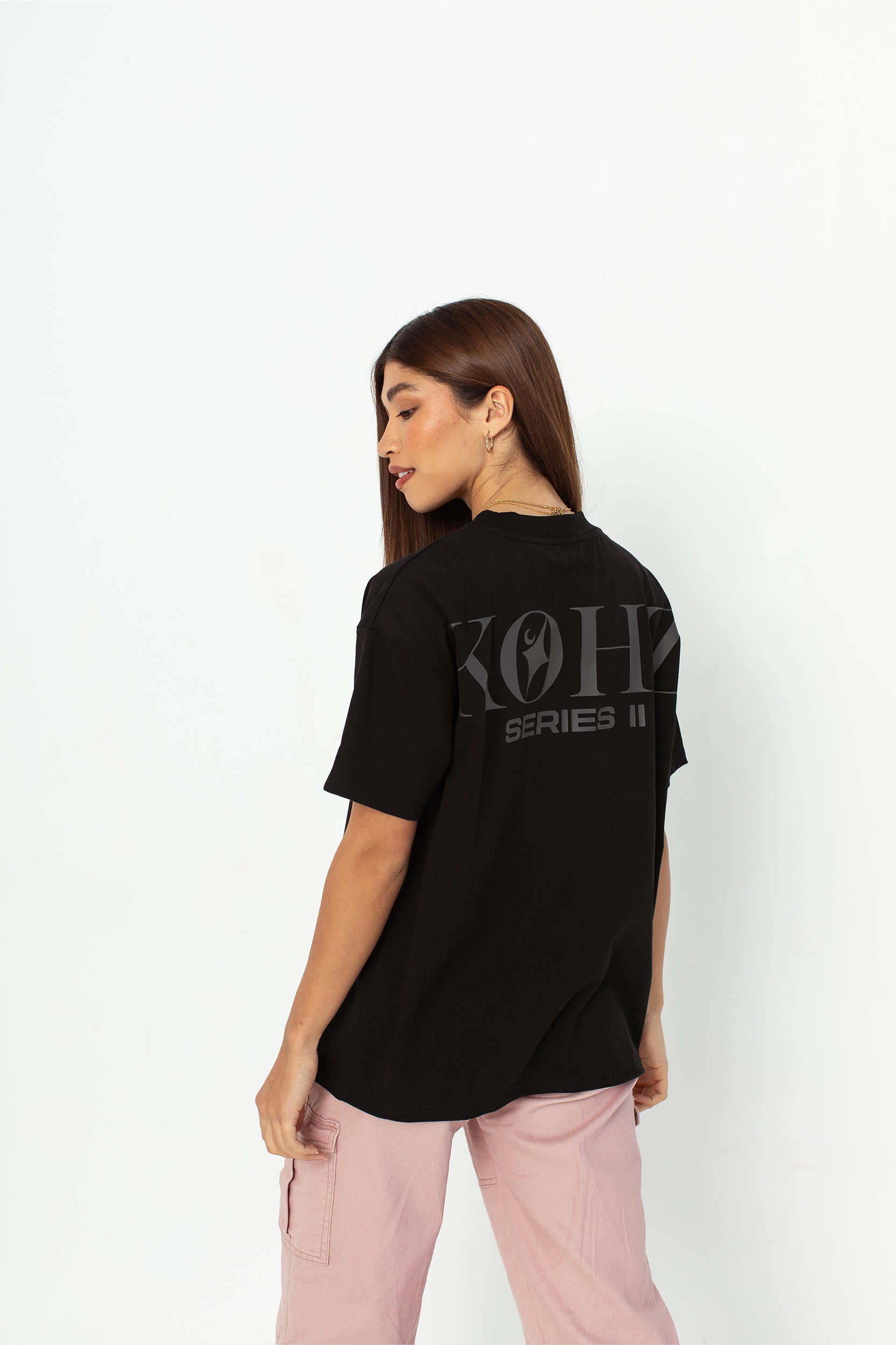 A model wearing a black oversized kohz  t-shirt with a puff printed logo, crew neck, and short sleeves standing against a white background.