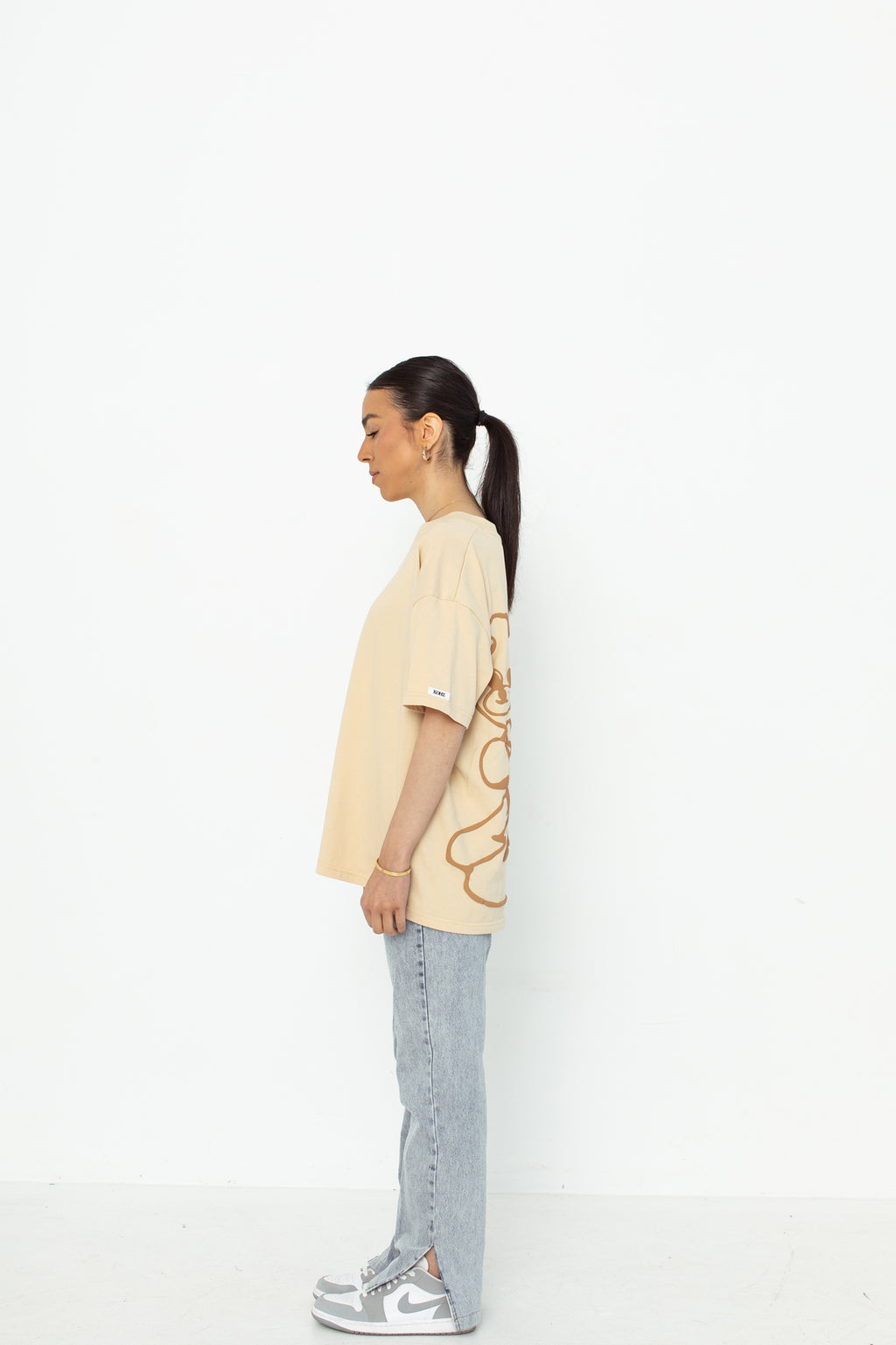 A model wearing a white oversized kohz bb t-shirt with a puff printed logo, crew neck, and short sleeves standing against a white background.
