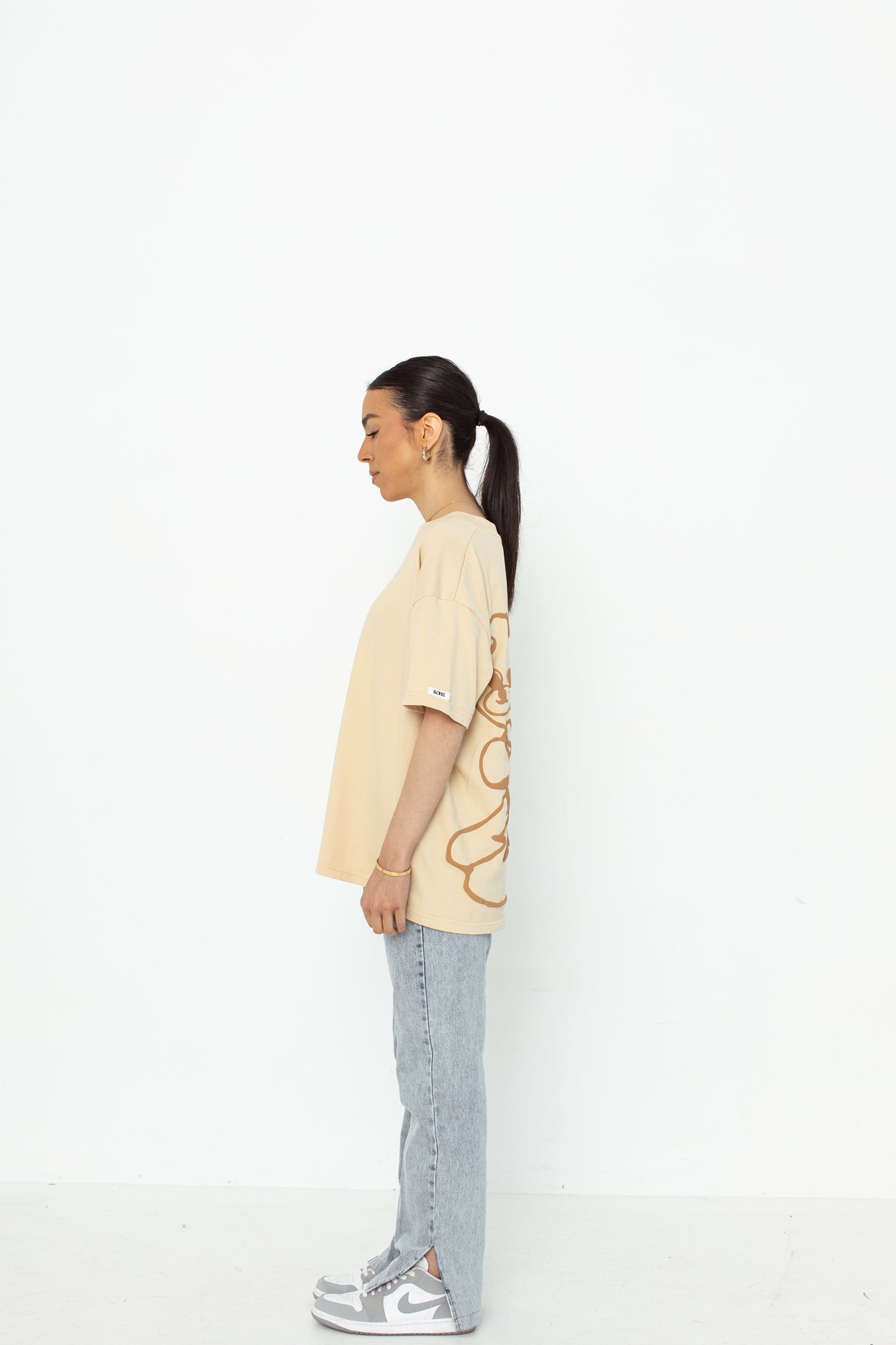 A model wearing a white oversized kohz bb t-shirt with a puff printed logo, crew neck, and short sleeves standing against a white background.