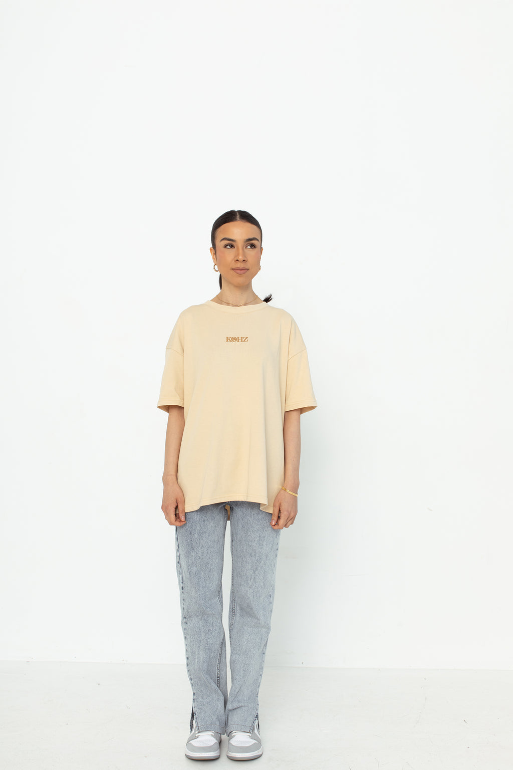 A model wearing a white oversized kohz bb t-shirt with a puff printed logo, crew neck, and short sleeves standing against a white background.