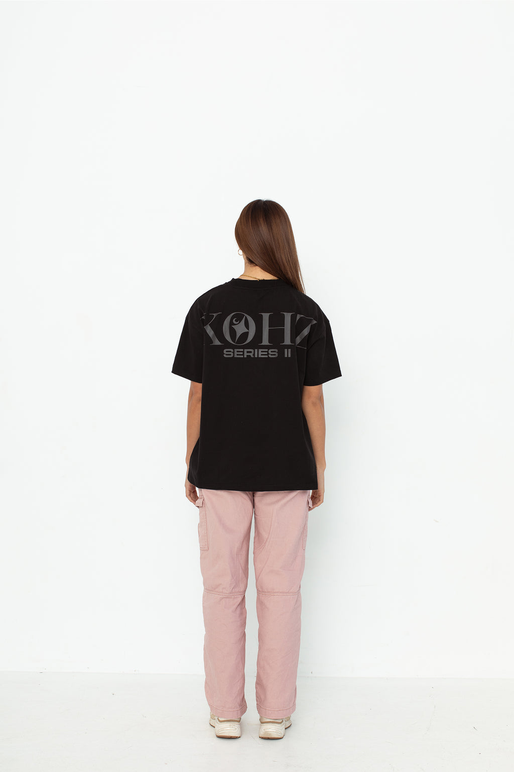 A model wearing a black oversized kohz  t-shirt with a puff printed logo, crew neck, and short sleeves standing against a white background.