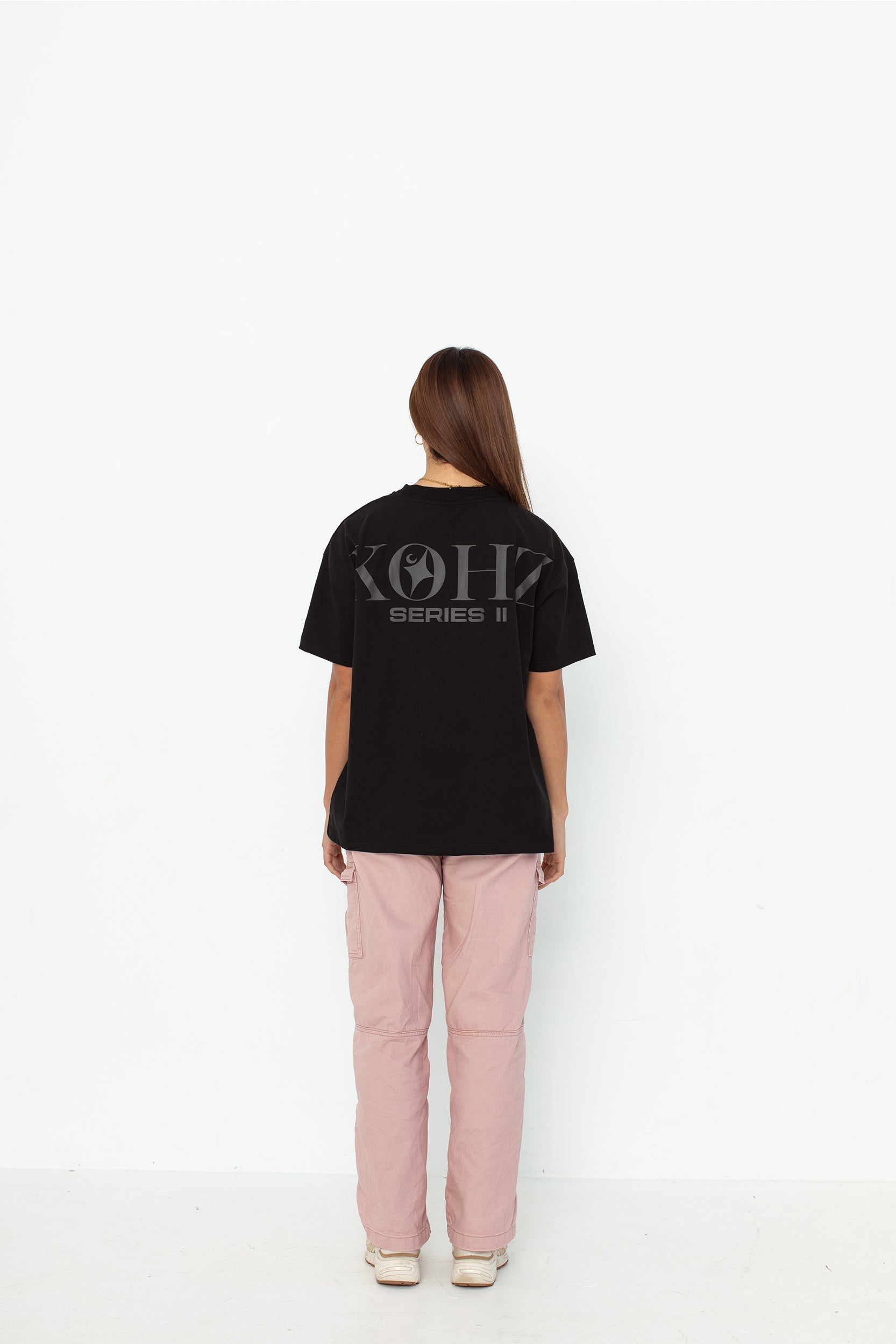A model wearing a black oversized kohz  t-shirt with a puff printed logo, crew neck, and short sleeves standing against a white background.