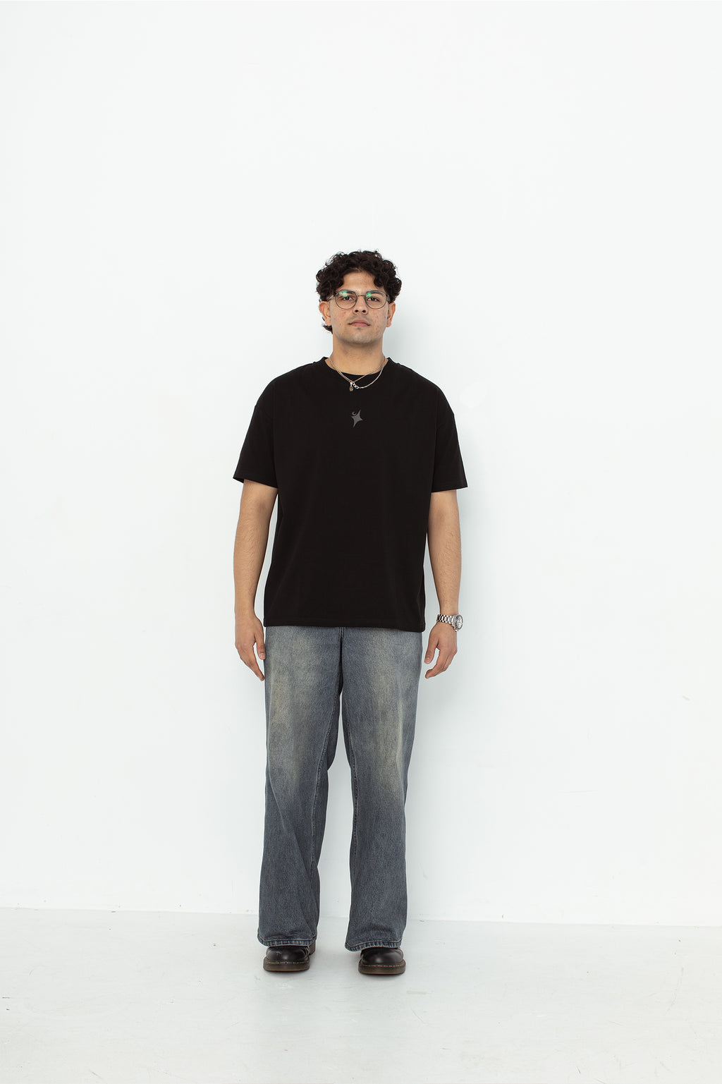 A model wearing a black oversized kohz  t-shirt with a puff printed logo, crew neck, and short sleeves standing against a white background.