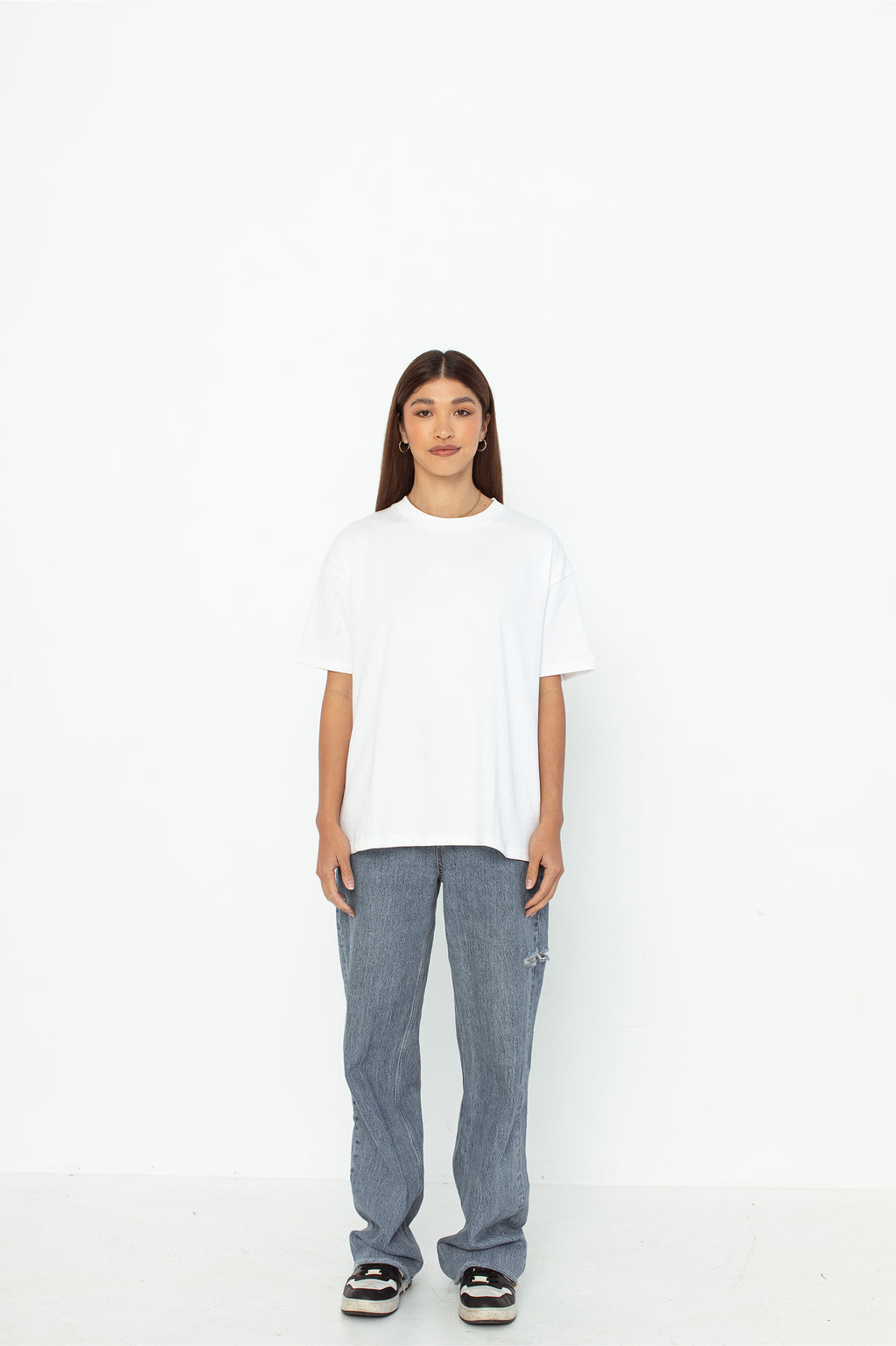 A model wearing a white oversized kohz bb t-shirt with a puff printed logo, crew neck, and short sleeves standing against a white background.