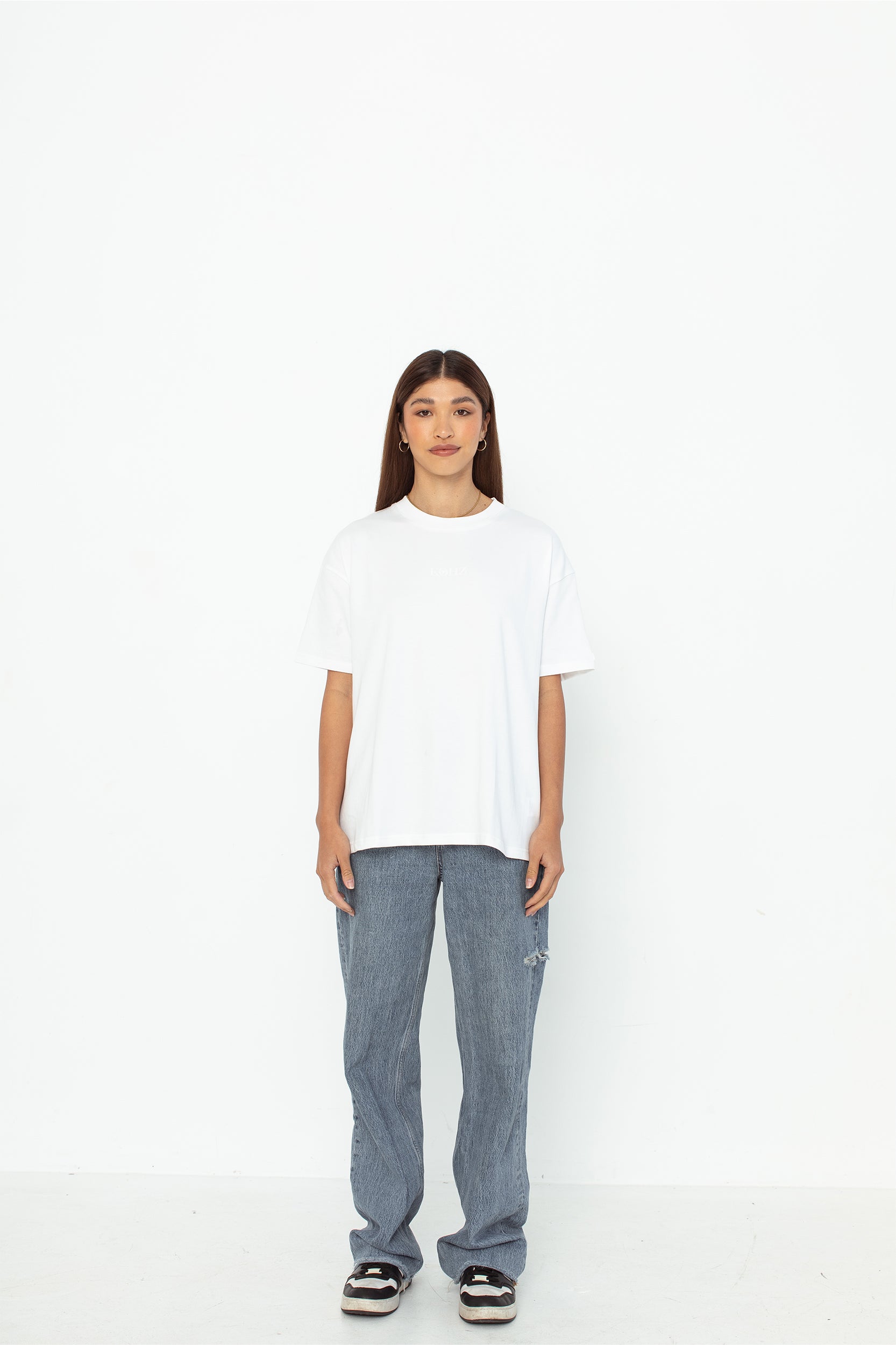 A model wearing a white oversized kohz bb t-shirt with a puff printed logo, crew neck, and short sleeves standing against a white background.