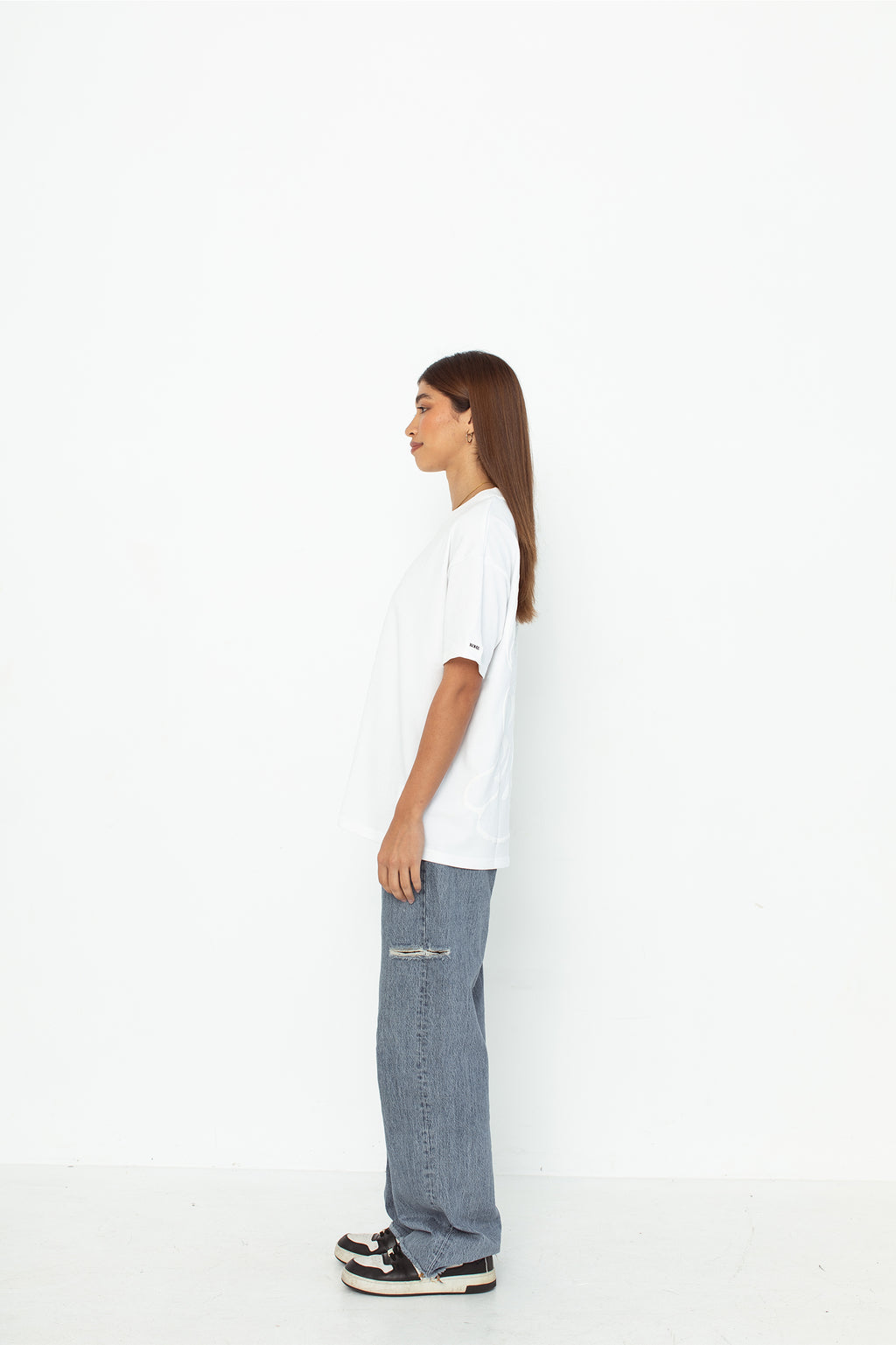 A model wearing a white oversized kohz bb t-shirt with a puff printed logo, crew neck, and short sleeves standing against a white background.