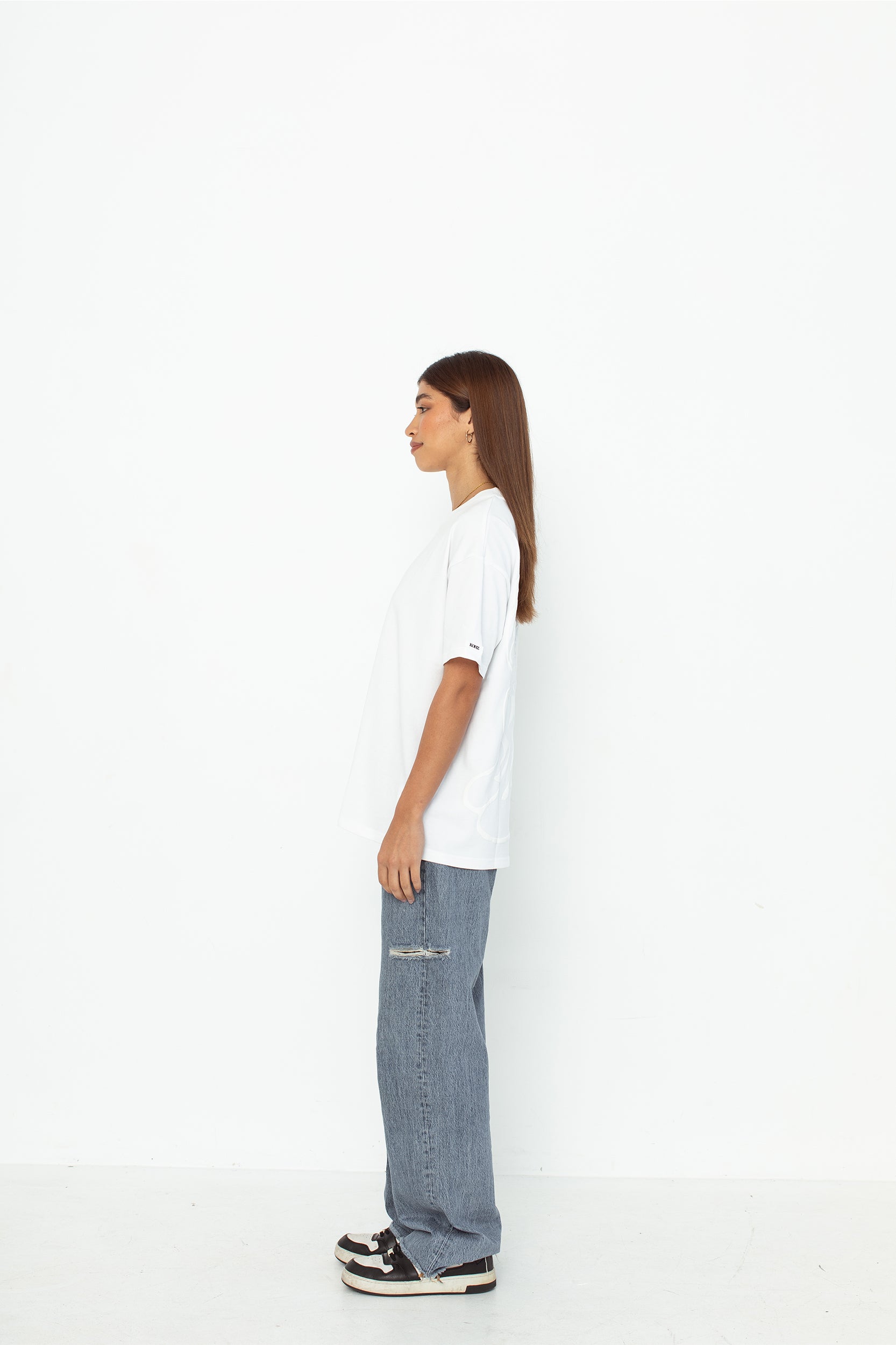A model wearing a white oversized kohz bb t-shirt with a puff printed logo, crew neck, and short sleeves standing against a white background.