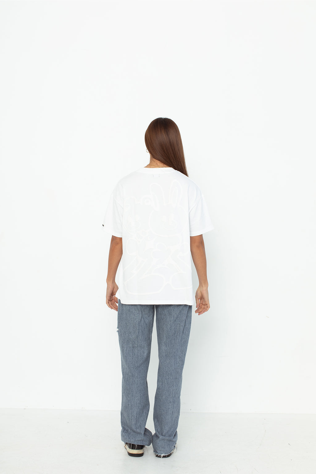 A model wearing a white oversized kohz bb t-shirt with a puff printed logo, crew neck, and short sleeves standing against a white background.