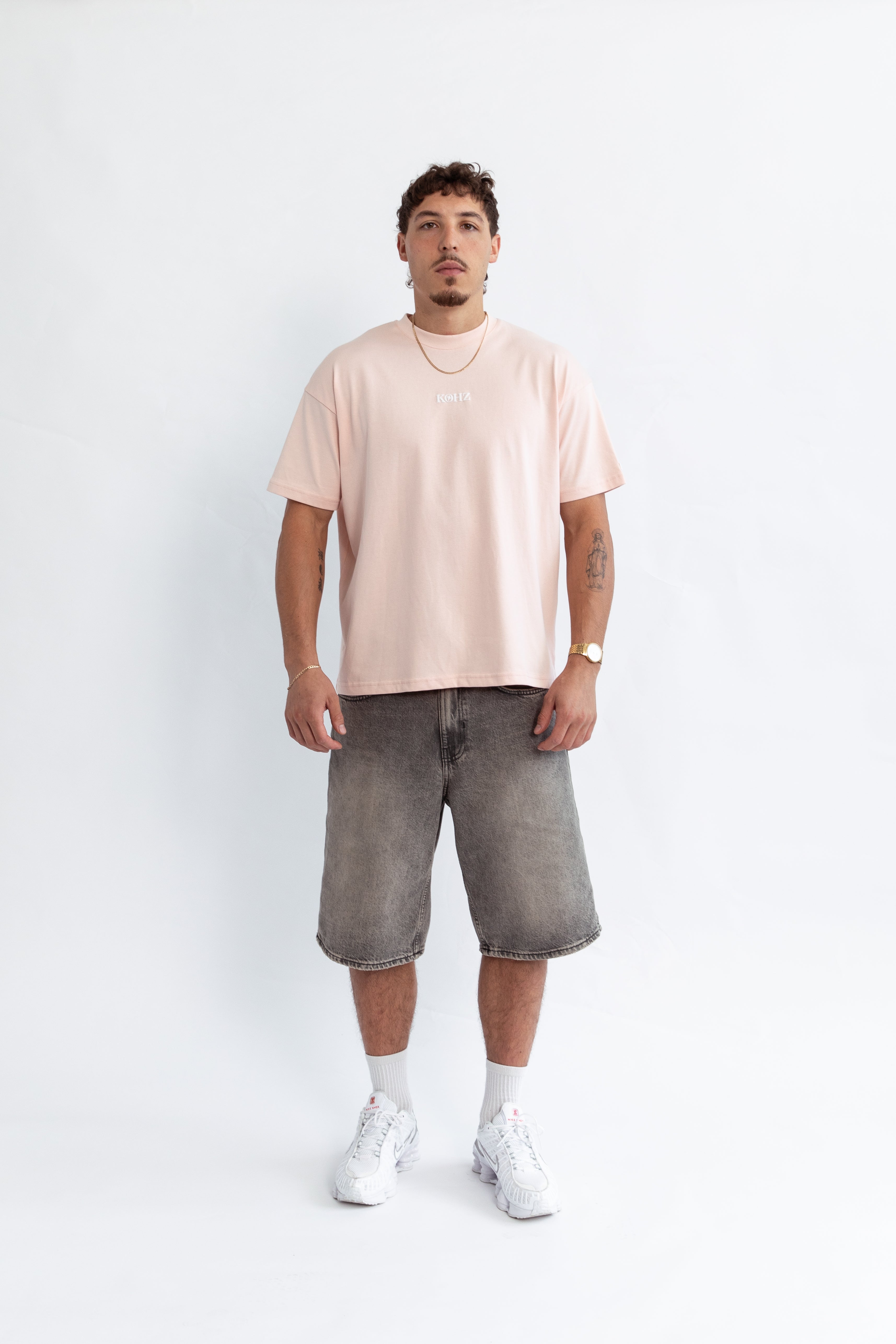 A model wearing a pink oversized kohz bb t-shirt with a puff printed logo, crew neck, and short sleeves standing against a white background.
