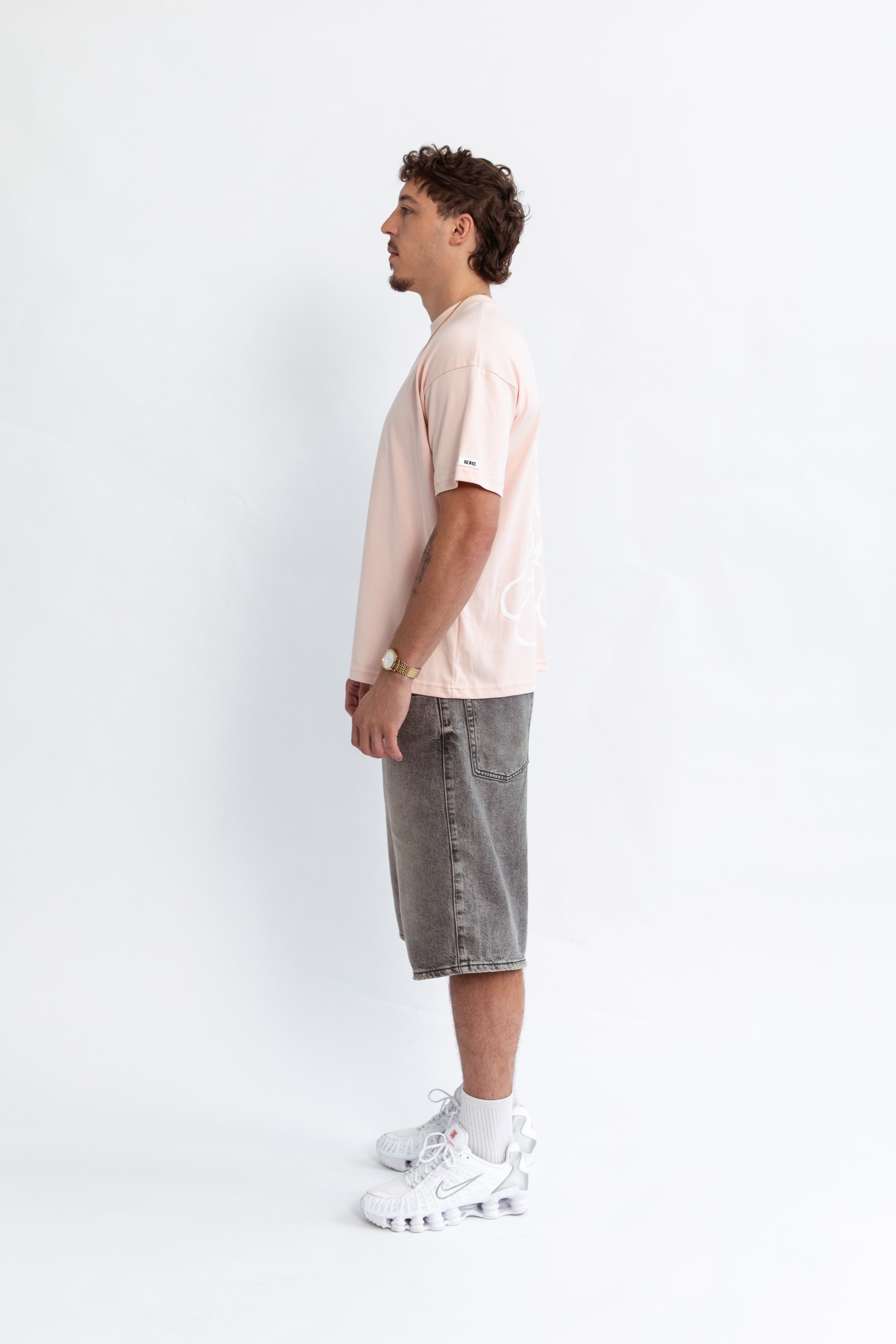 A model wearing a pink oversized kohz bb t-shirt with a puff printed logo, crew neck, and short sleeves standing against a white background.