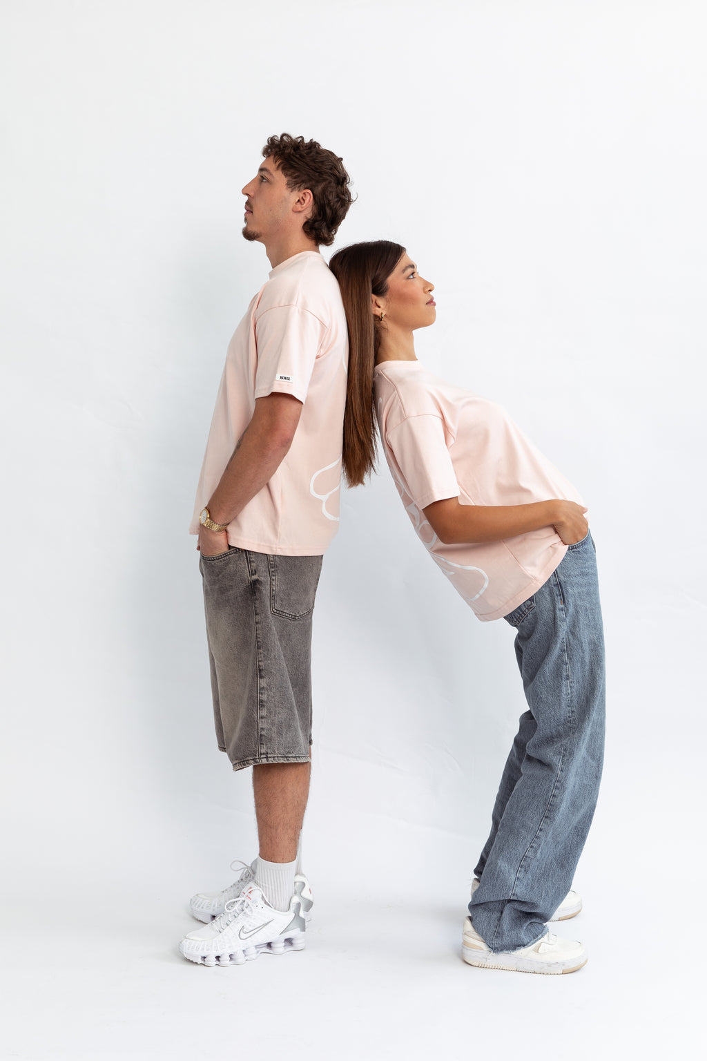 two models wearing a pink oversized kohz bb t-shirt with a puff printed logo, crew neck, and short sleeves standing against a white background.