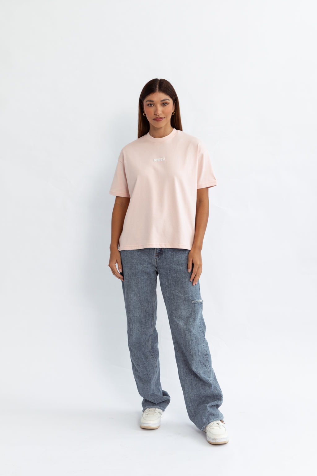 A model wearing a pink oversized kohz bb t-shirt with a puff printed logo, crew neck, and short sleeves standing against a white background.