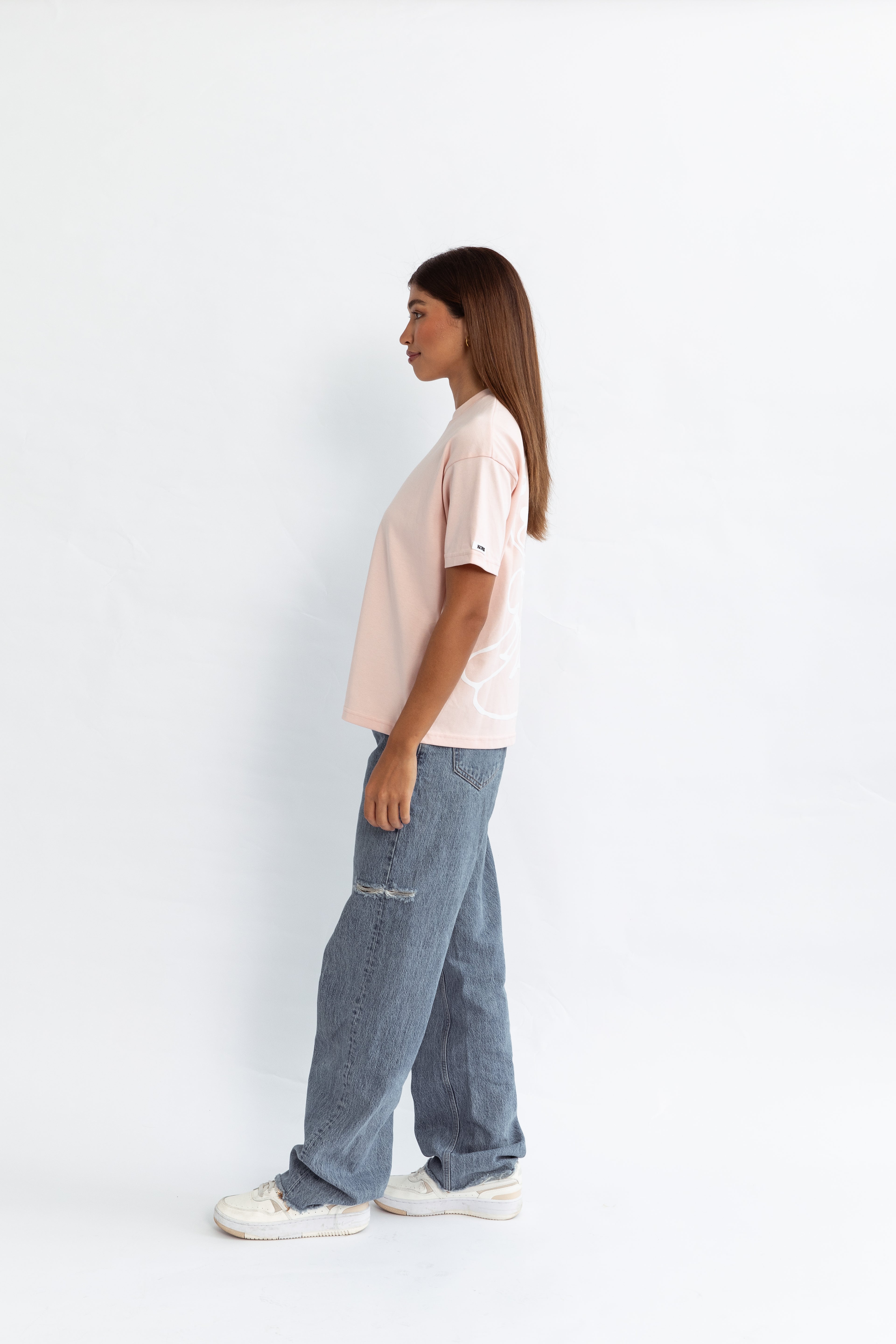 A model wearing a pink oversized kohz bb t-shirt with a puff printed logo, crew neck, and short sleeves standing against a white background.