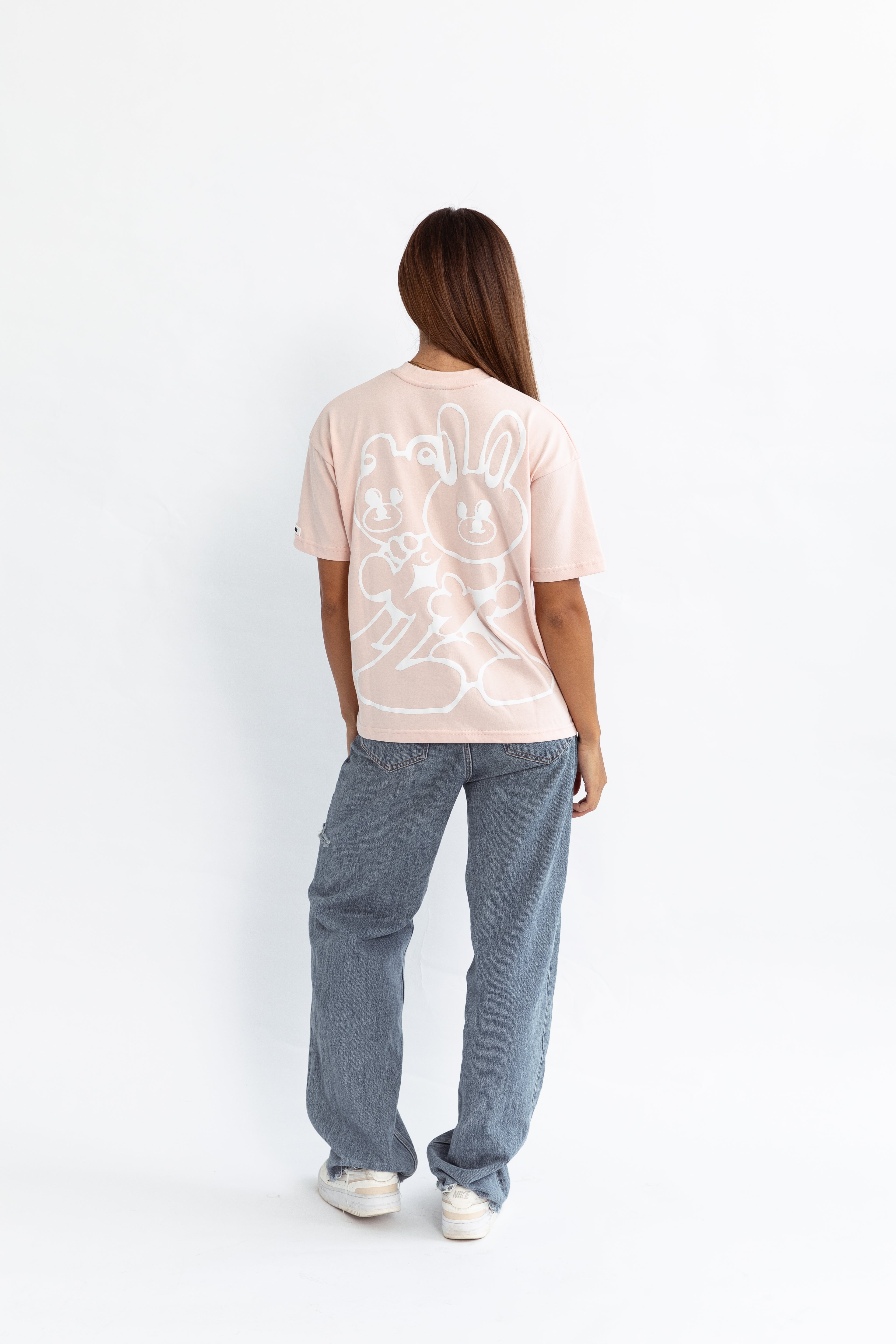 A model wearing a pink oversized kohz bb t-shirt with a puff printed logo, crew neck, and short sleeves standing against a white background.