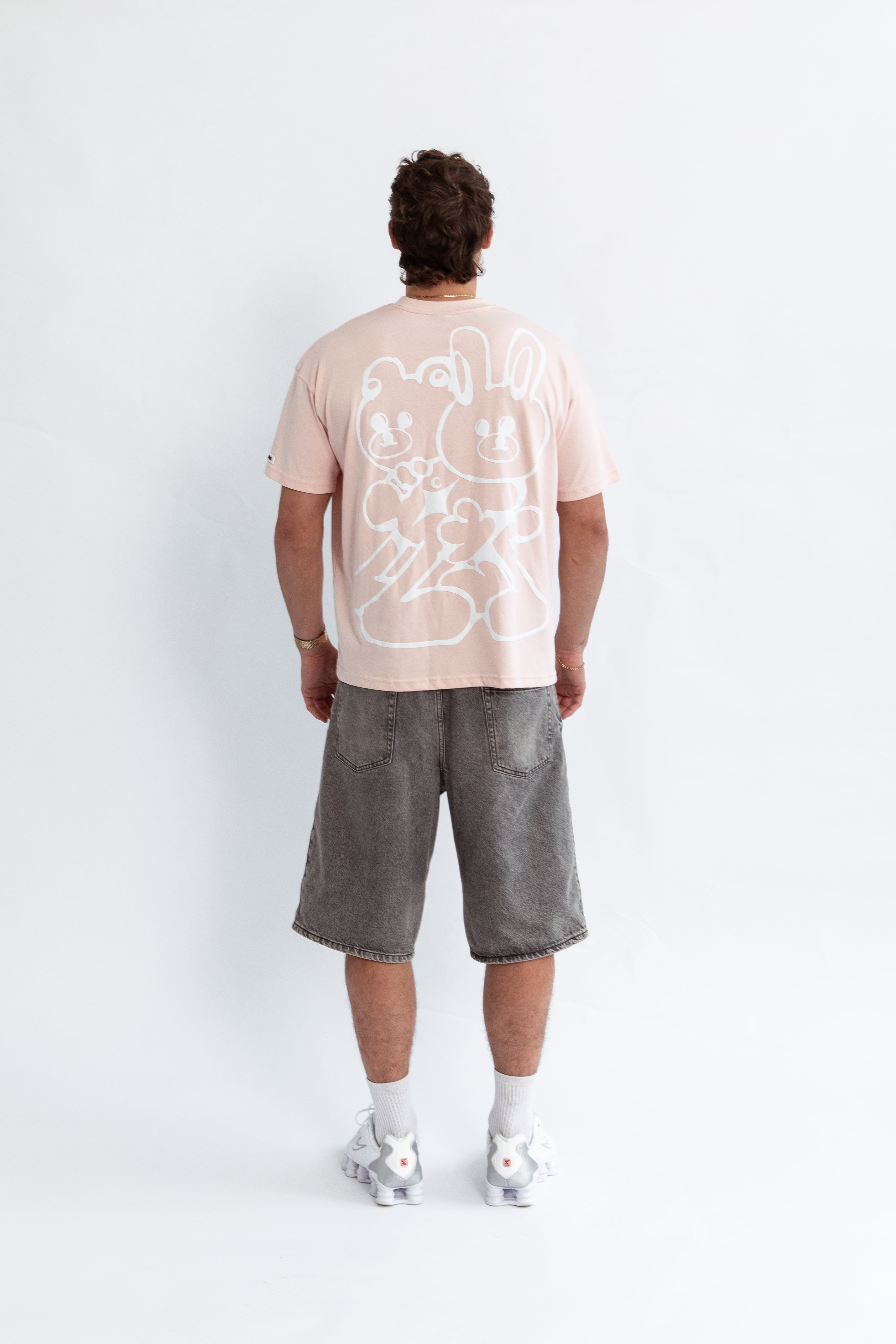 A model wearing a pink oversized kohz bb t-shirt with a puff printed logo, crew neck, and short sleeves standing against a white background.