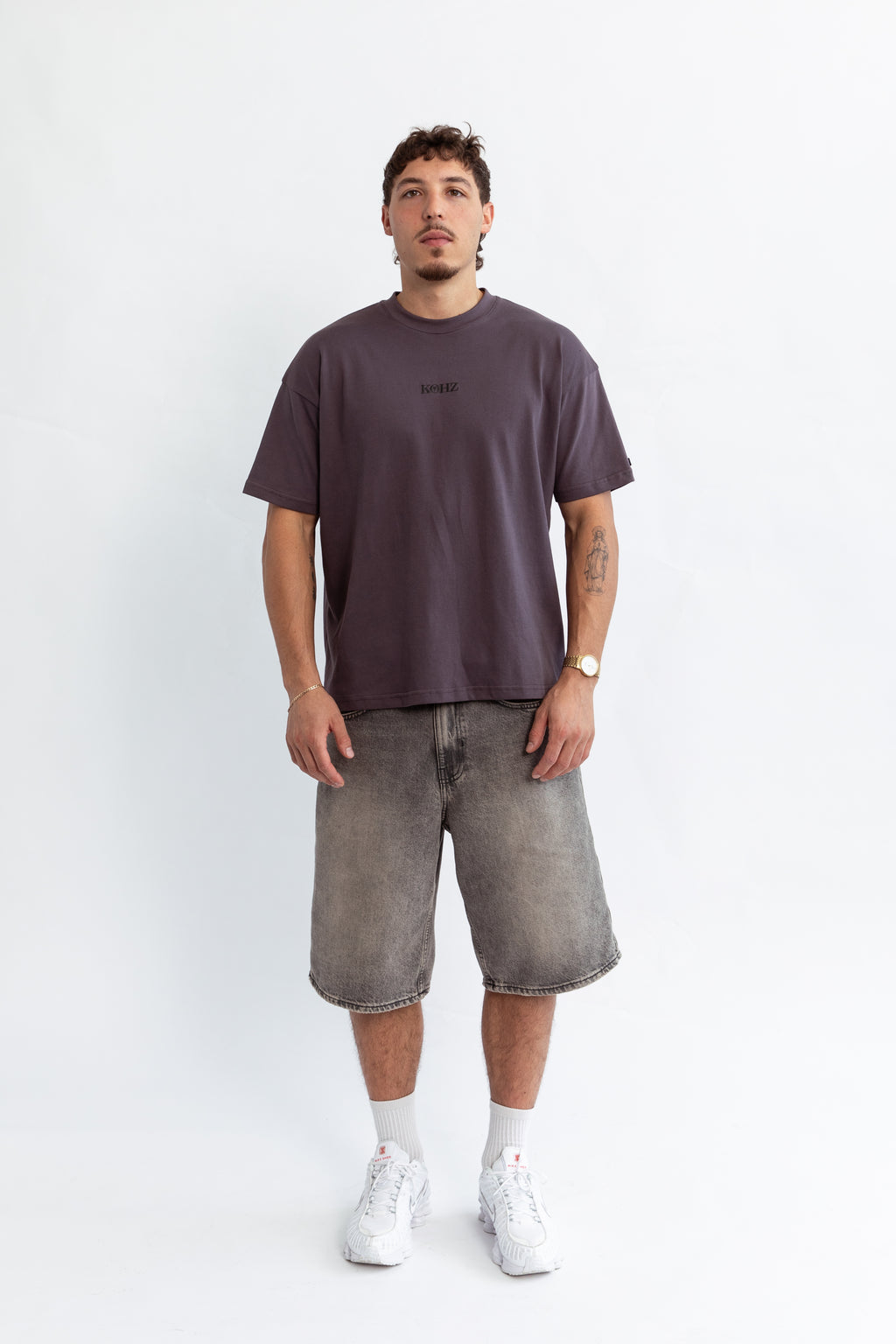 A model wearing a grey oversized kohz bb t-shirt with a puff printed logo, crew neck, and short sleeves standing against a white background.