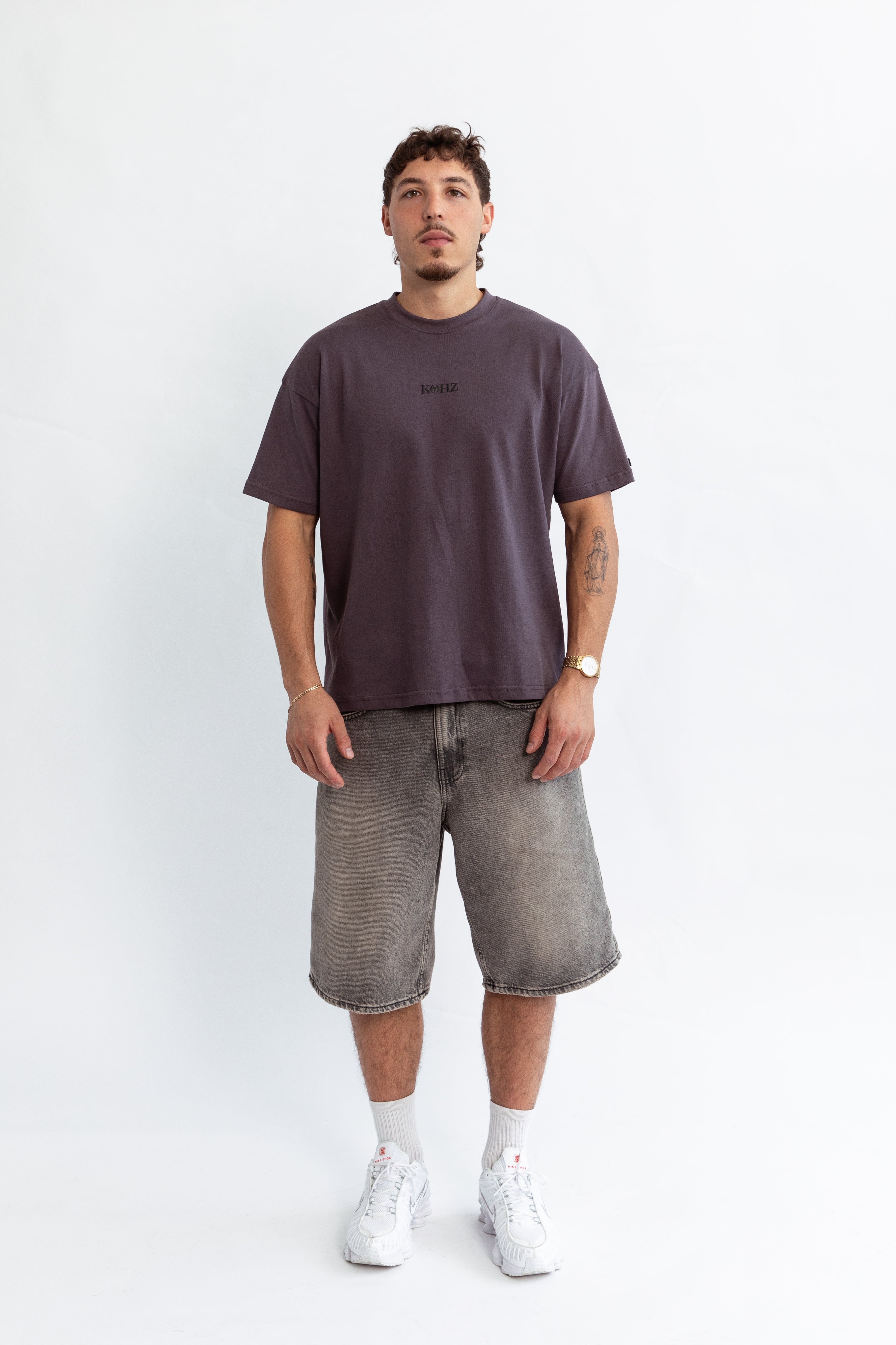 A model wearing a grey oversized kohz bb t-shirt with a puff printed logo, crew neck, and short sleeves standing against a white background.