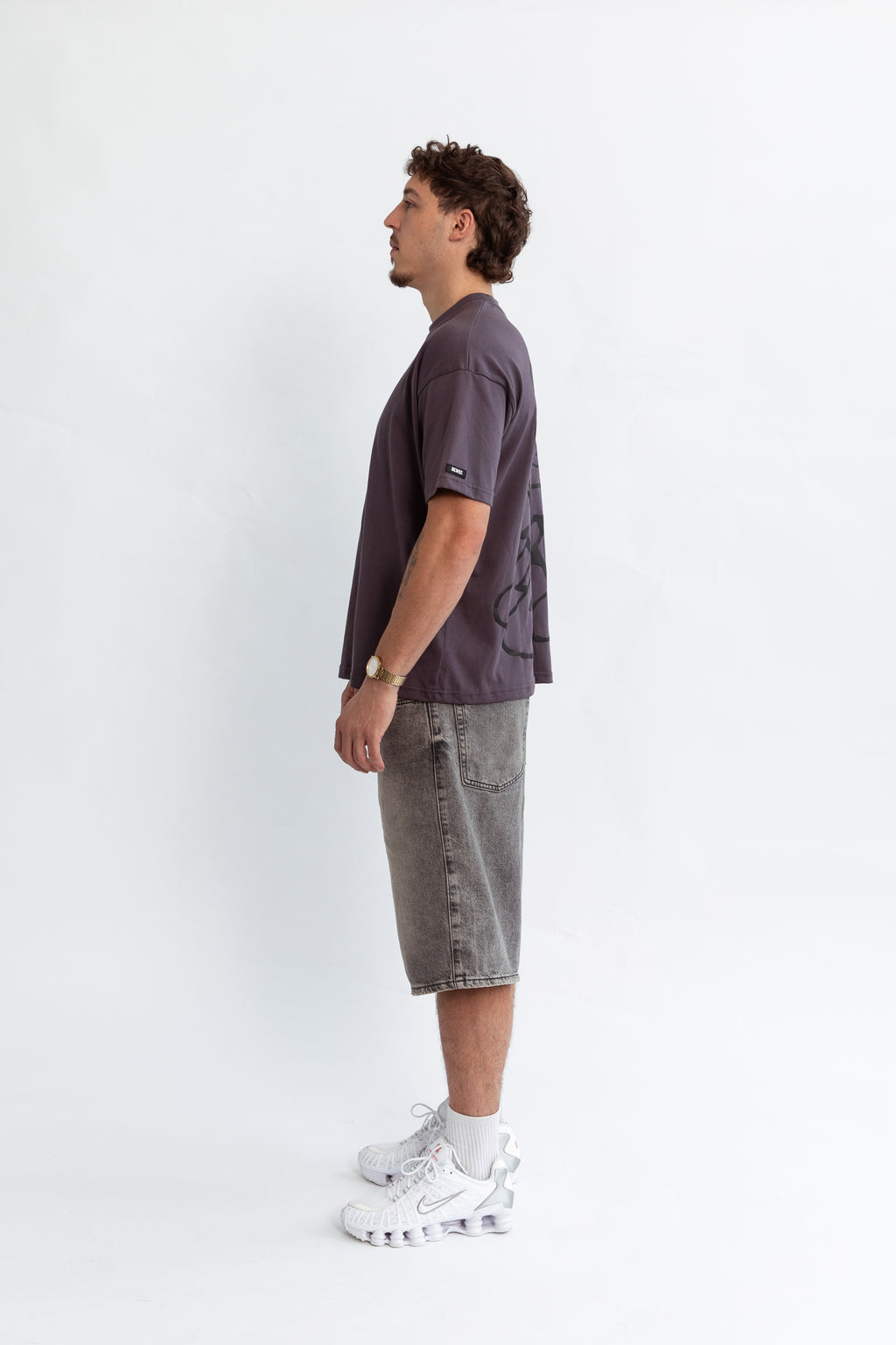 A model wearing a grey oversized kohz bb t-shirt with a puff printed logo, crew neck, and short sleeves standing against a white background.