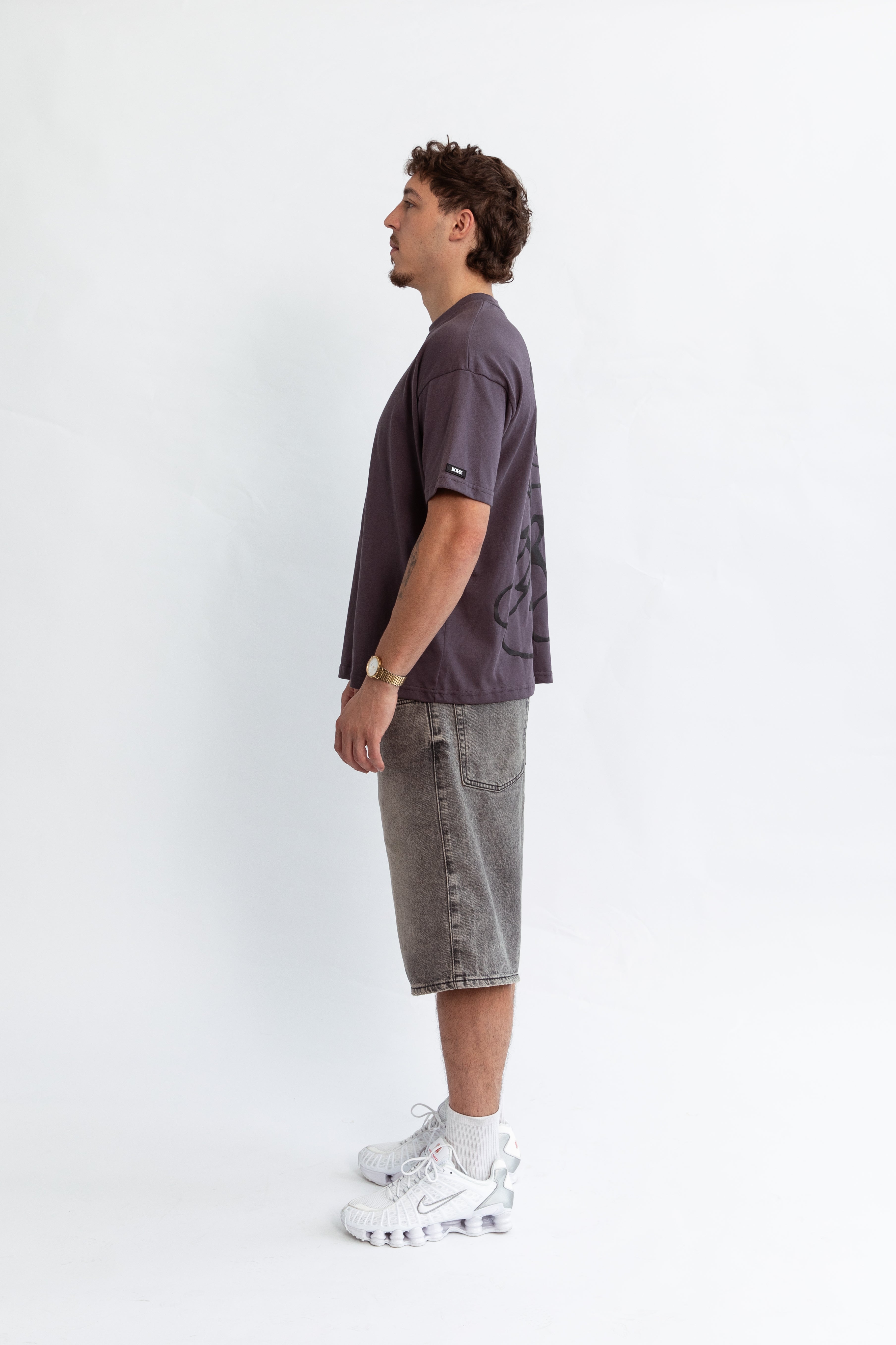A model wearing a grey oversized kohz bb t-shirt with a puff printed logo, crew neck, and short sleeves standing against a white background.