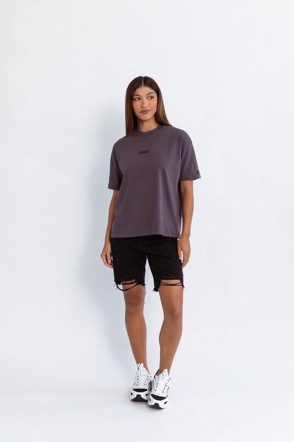 A model wearing a grey oversized kohz bb t-shirt with a puff printed logo, crew neck, and short sleeves standing against a white background.