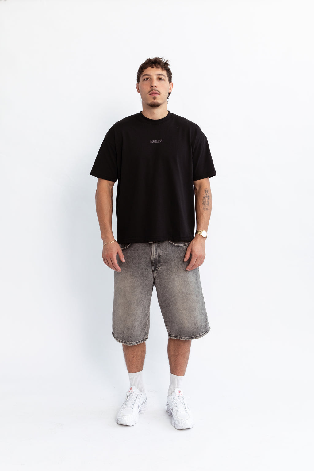 A person wearing a black oversized t-shirt with a puff printed logo, crew neck, and short sleeves standing against a white background.