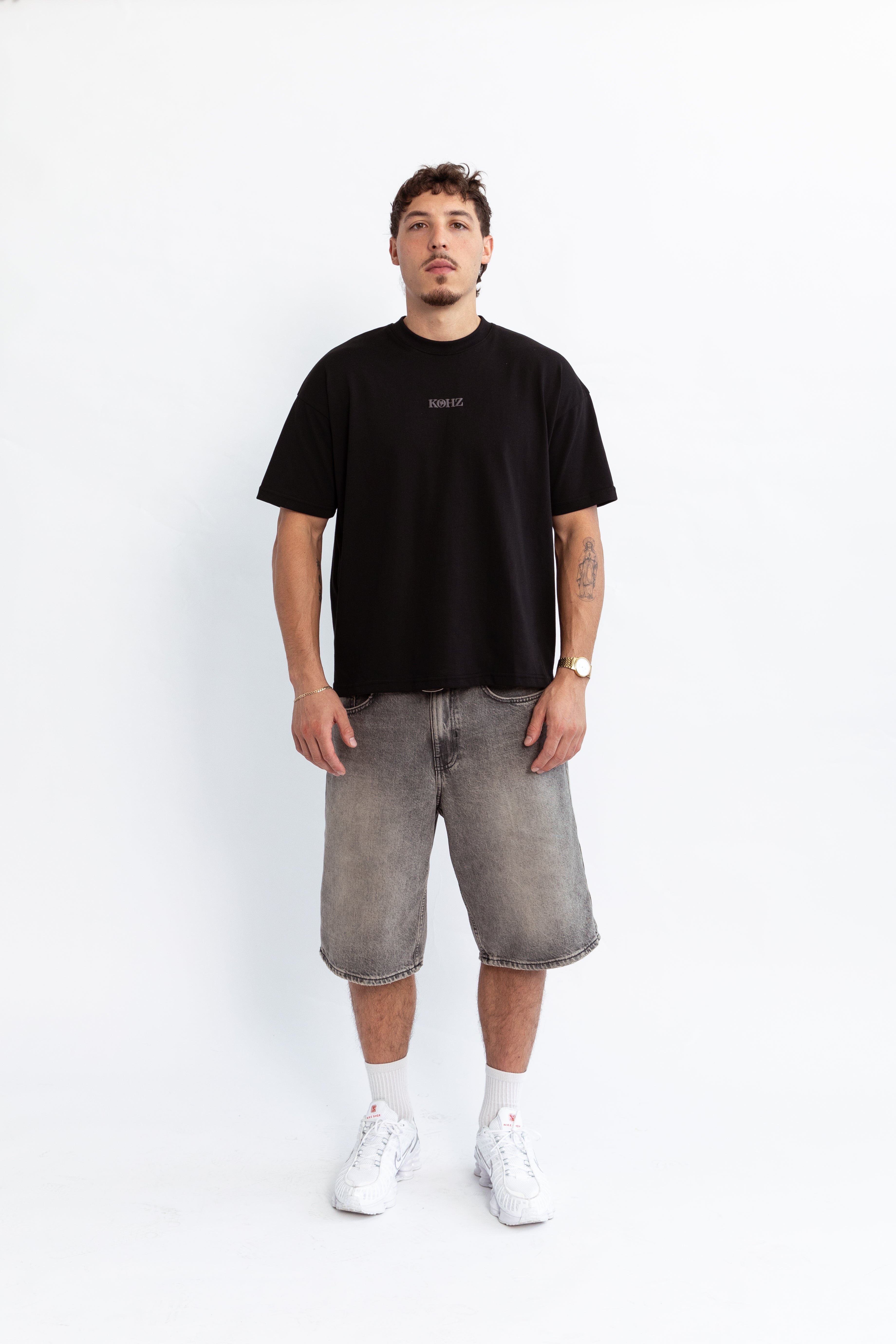 A person wearing a black oversized t-shirt with a puff printed logo, crew neck, and short sleeves standing against a white background.