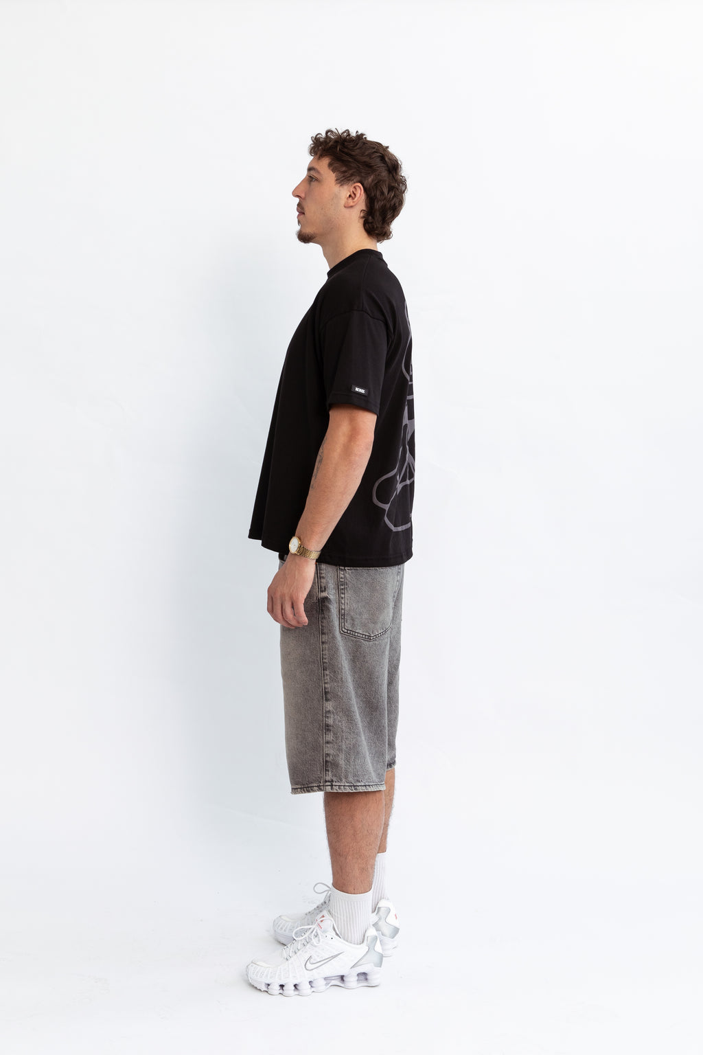 A model wearing a black oversized kohz bb t-shirt with a puff printed logo, crew neck, and short sleeves standing against a white background.