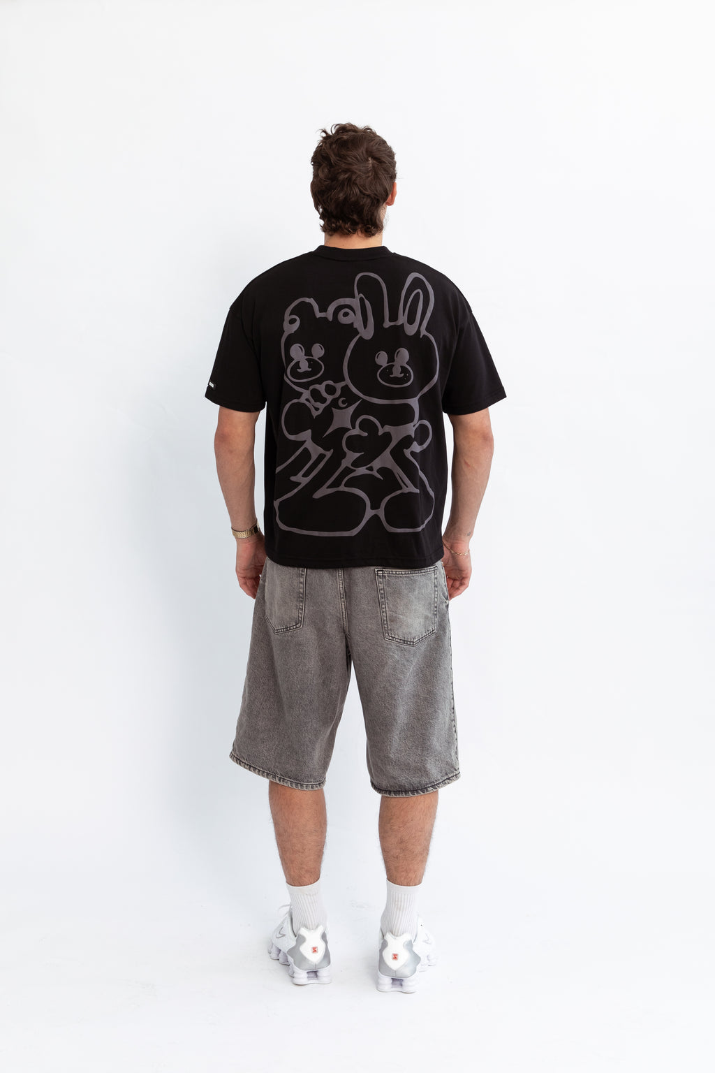 A model wearing a black oversized kohz bb t-shirt with a puff printed logo, crew neck, and short sleeves standing against a white background.