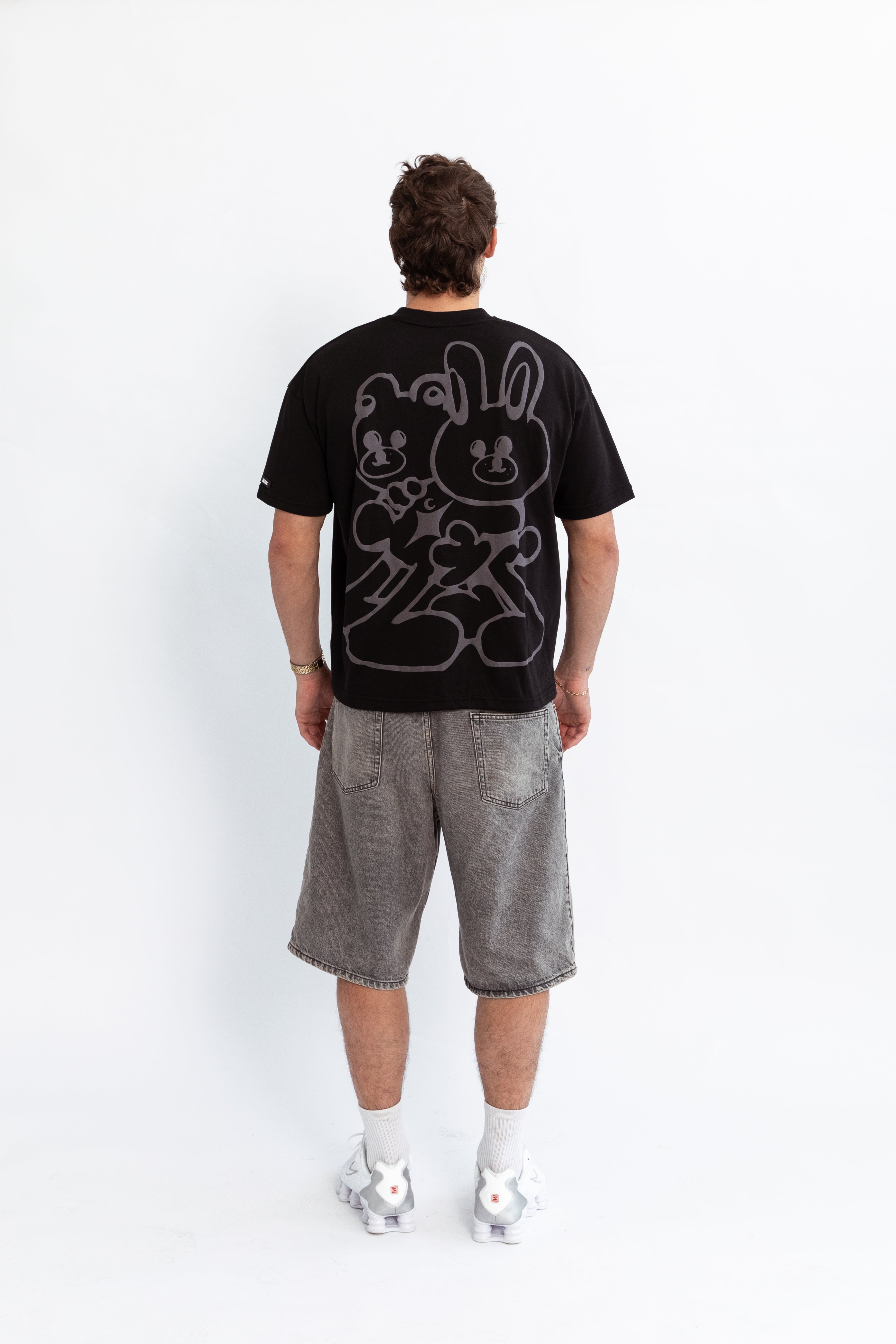 A model wearing a black oversized kohz bb t-shirt with a puff printed logo, crew neck, and short sleeves standing against a white background.