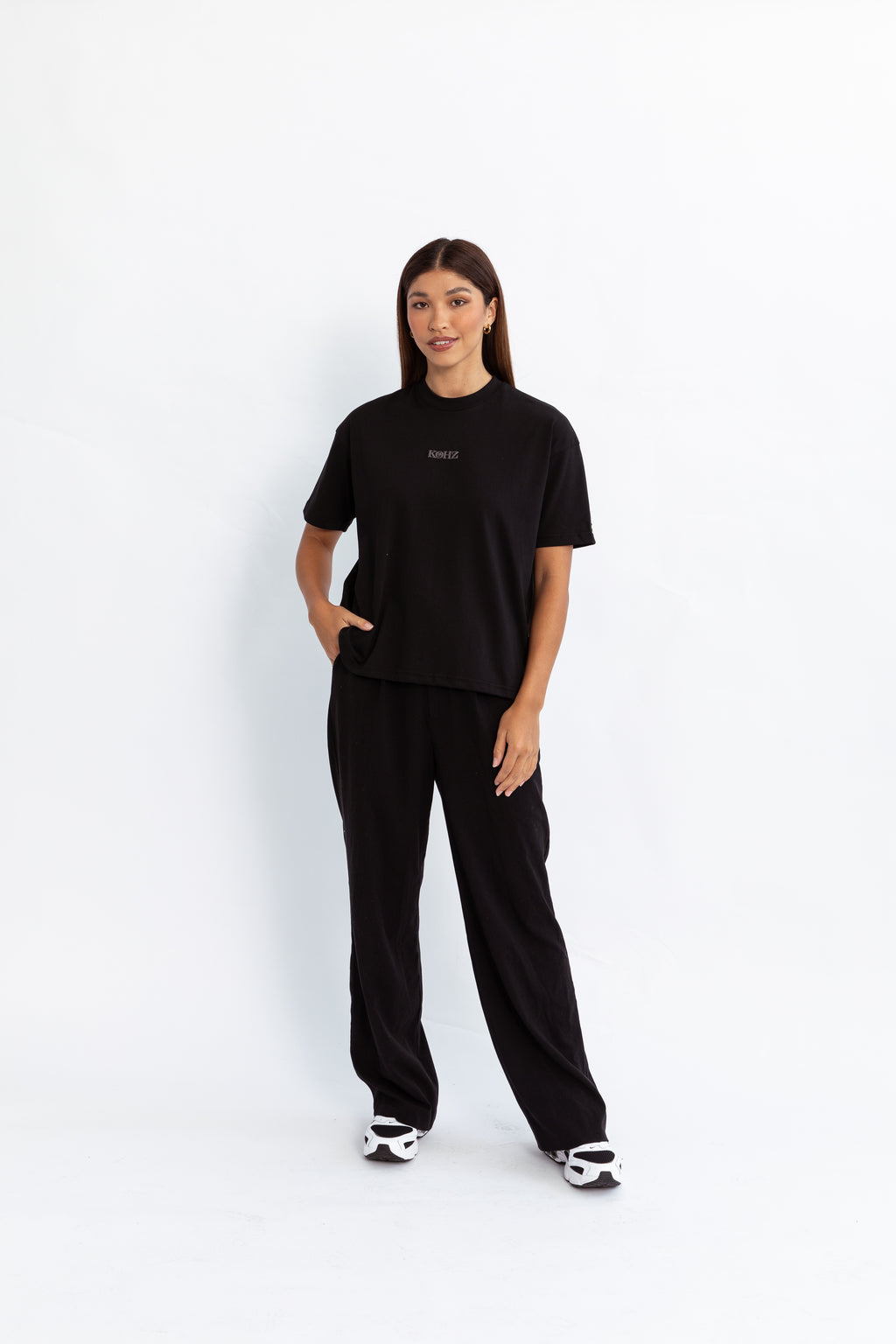 A model wearing a black oversized kohz bb t-shirt with a puff printed logo, crew neck, and short sleeves standing against a white background.