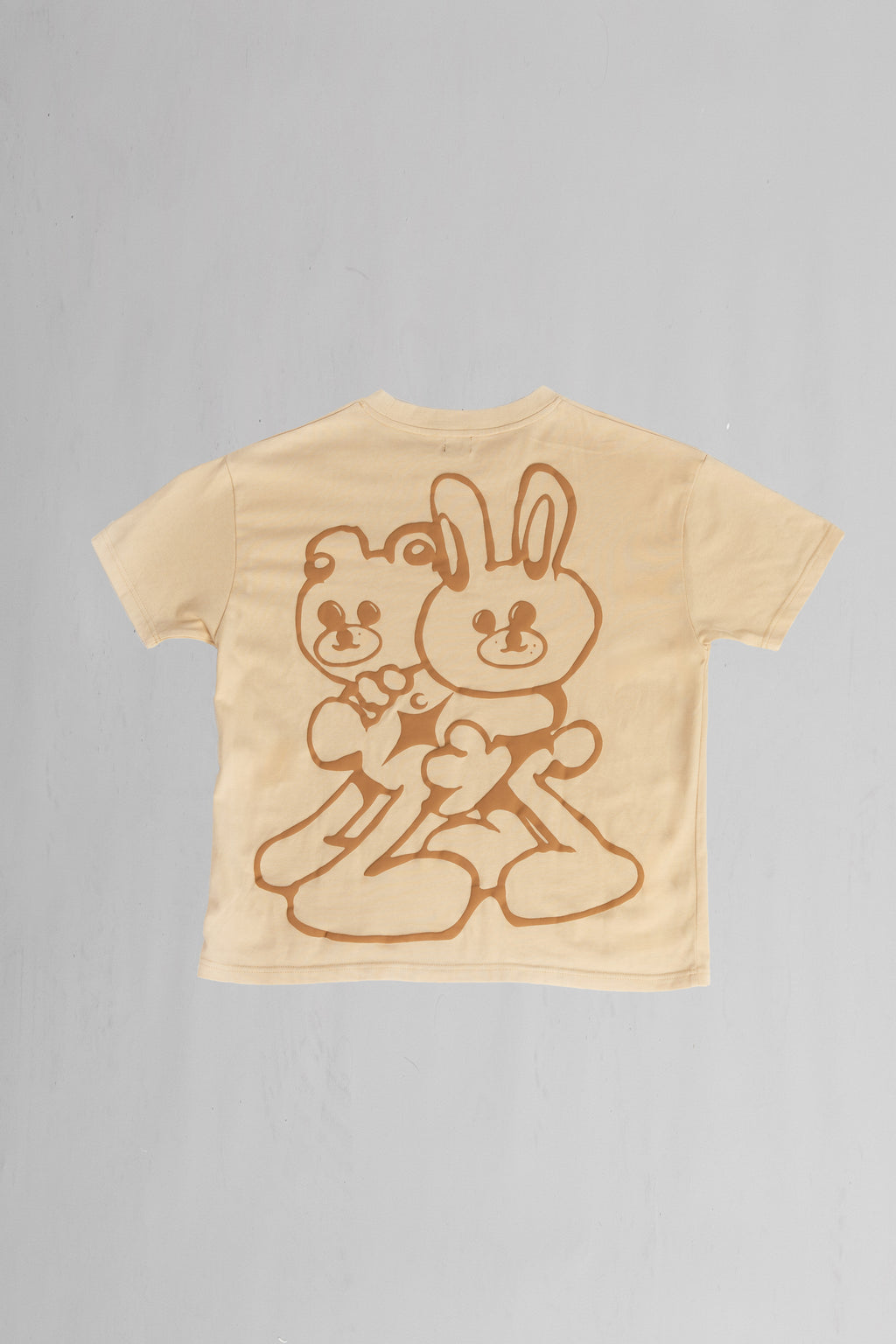 Back of beige oversized crewneck t-shirt with ribbed sleeves and a puff printed logo on the chest.