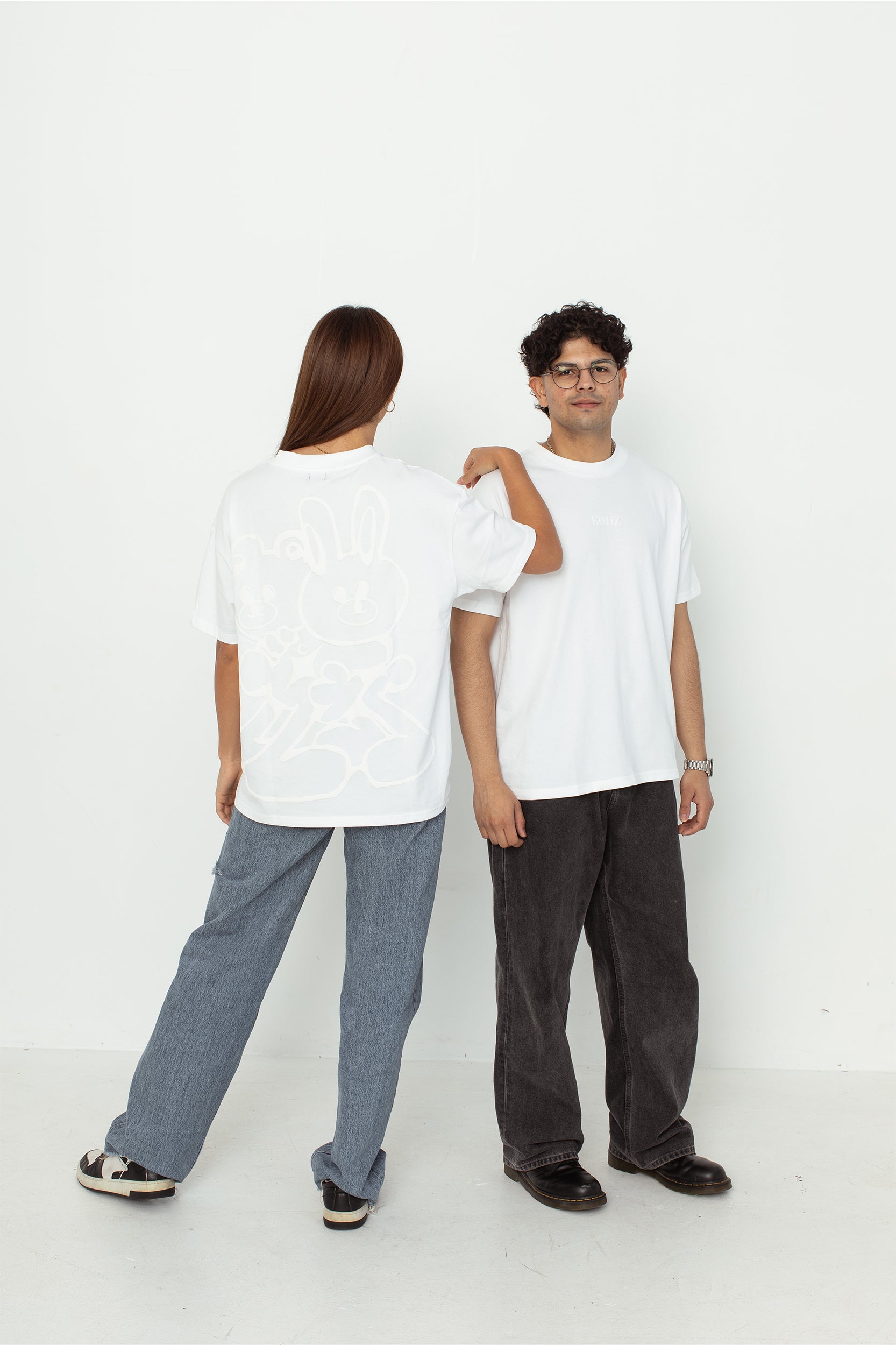 two models wearing a white oversized kohz bb t-shirt with a puff printed logo, crew neck, and short sleeves standing against a white background.