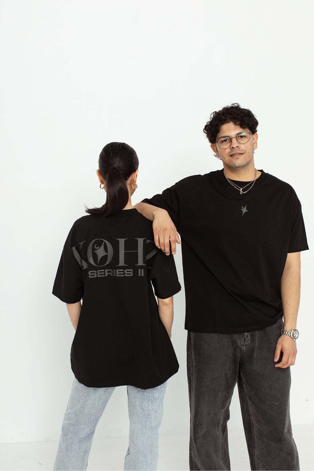two models wearing a black oversized kohz  t-shirt with a puff printed logo, crew neck, and short sleeves standing against a white background.